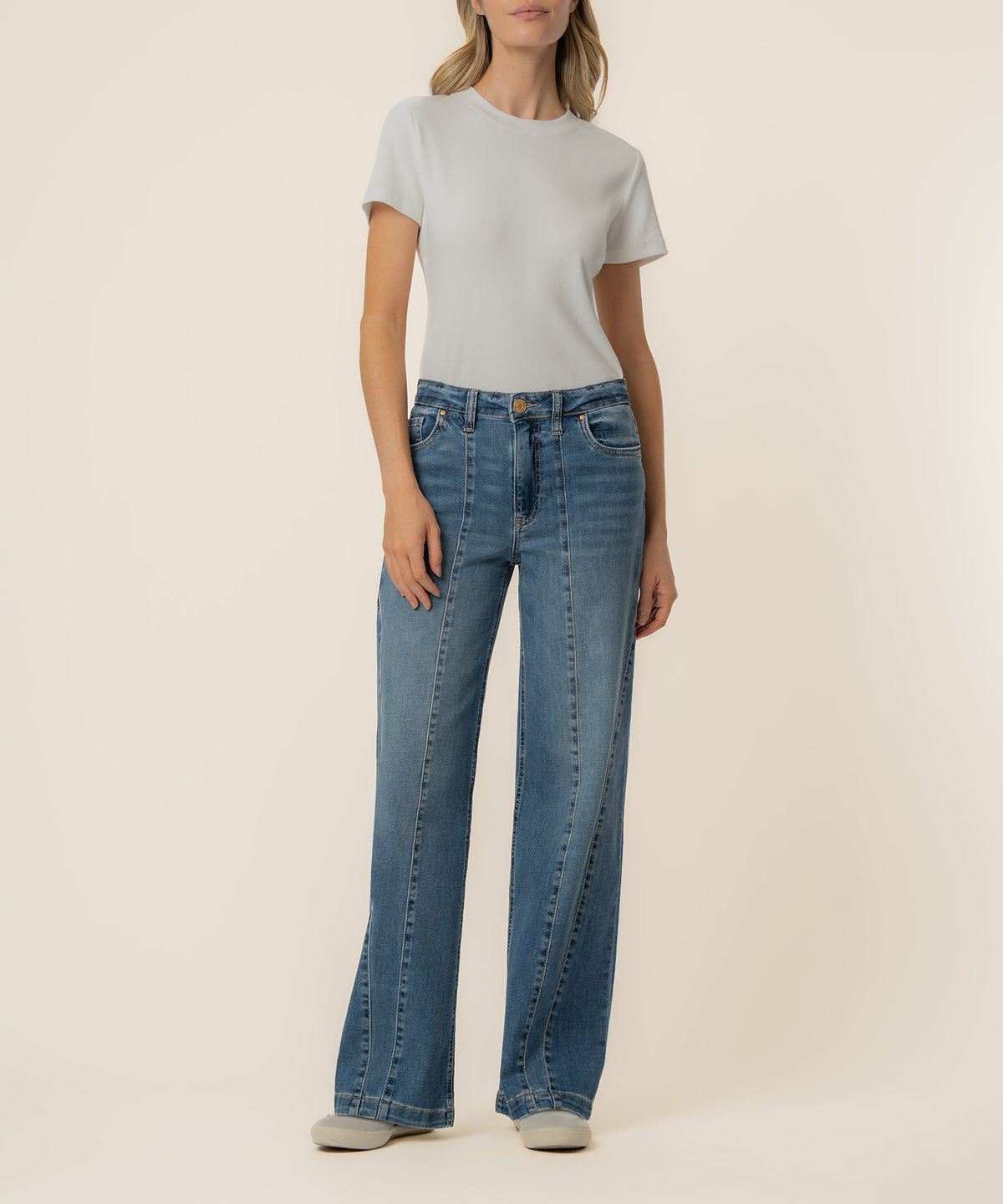 Woman wearing high-rise wide-leg blue jeans with a white t-shirt and white sneakers.