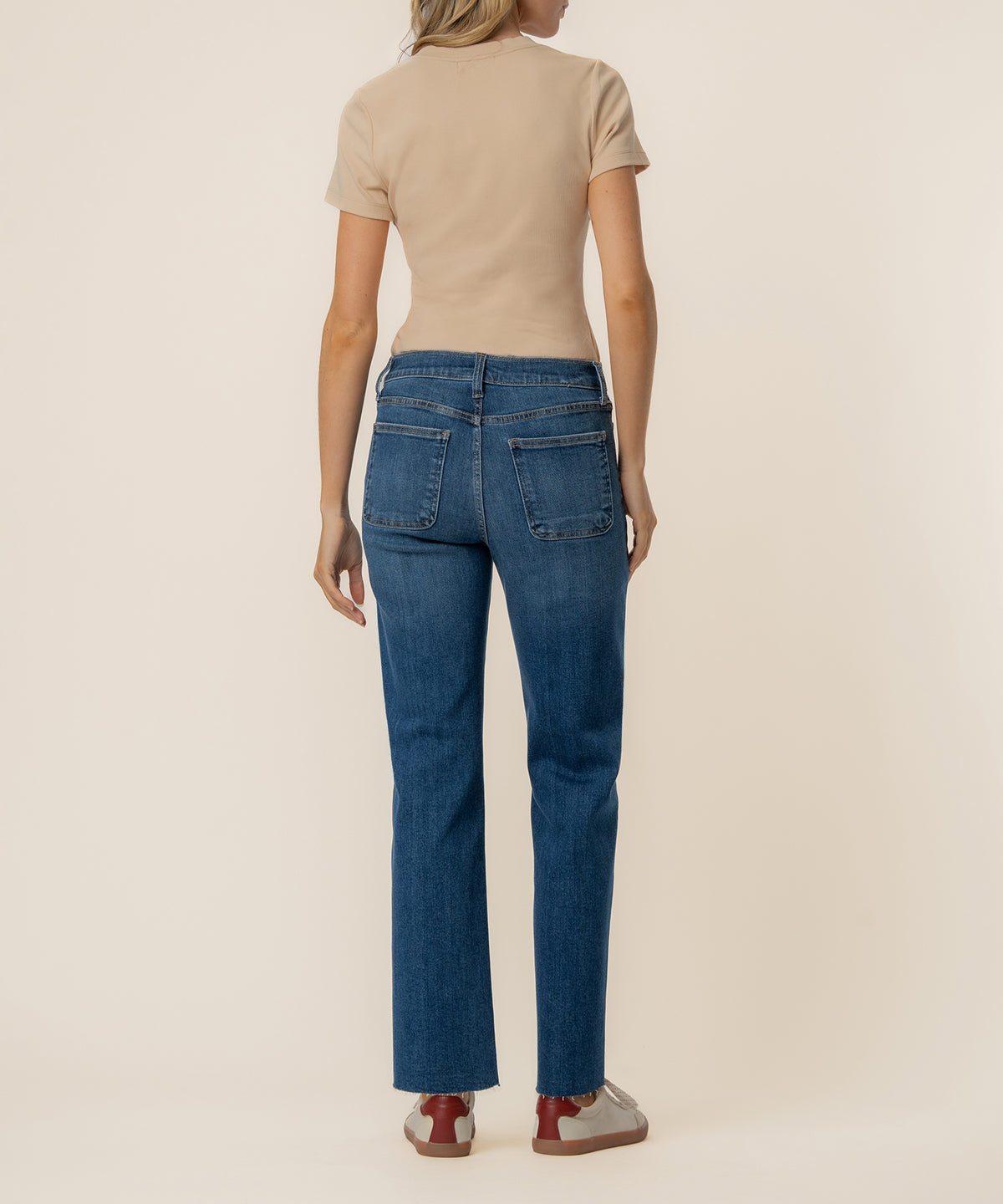 Woman wearing high-rise straight-leg jeans in medium blue denim with a beige t-shirt, rear view.