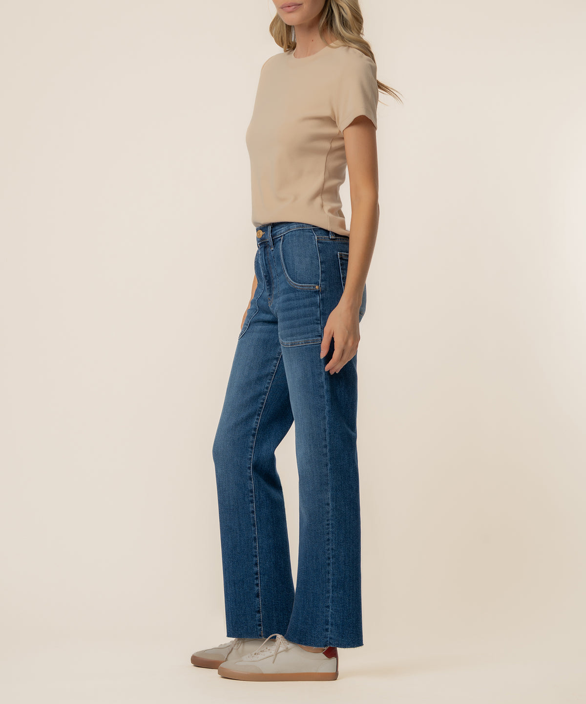Woman wearing beige short-sleeve t-shirt and blue high-rise straight leg jeans with white sneakers.