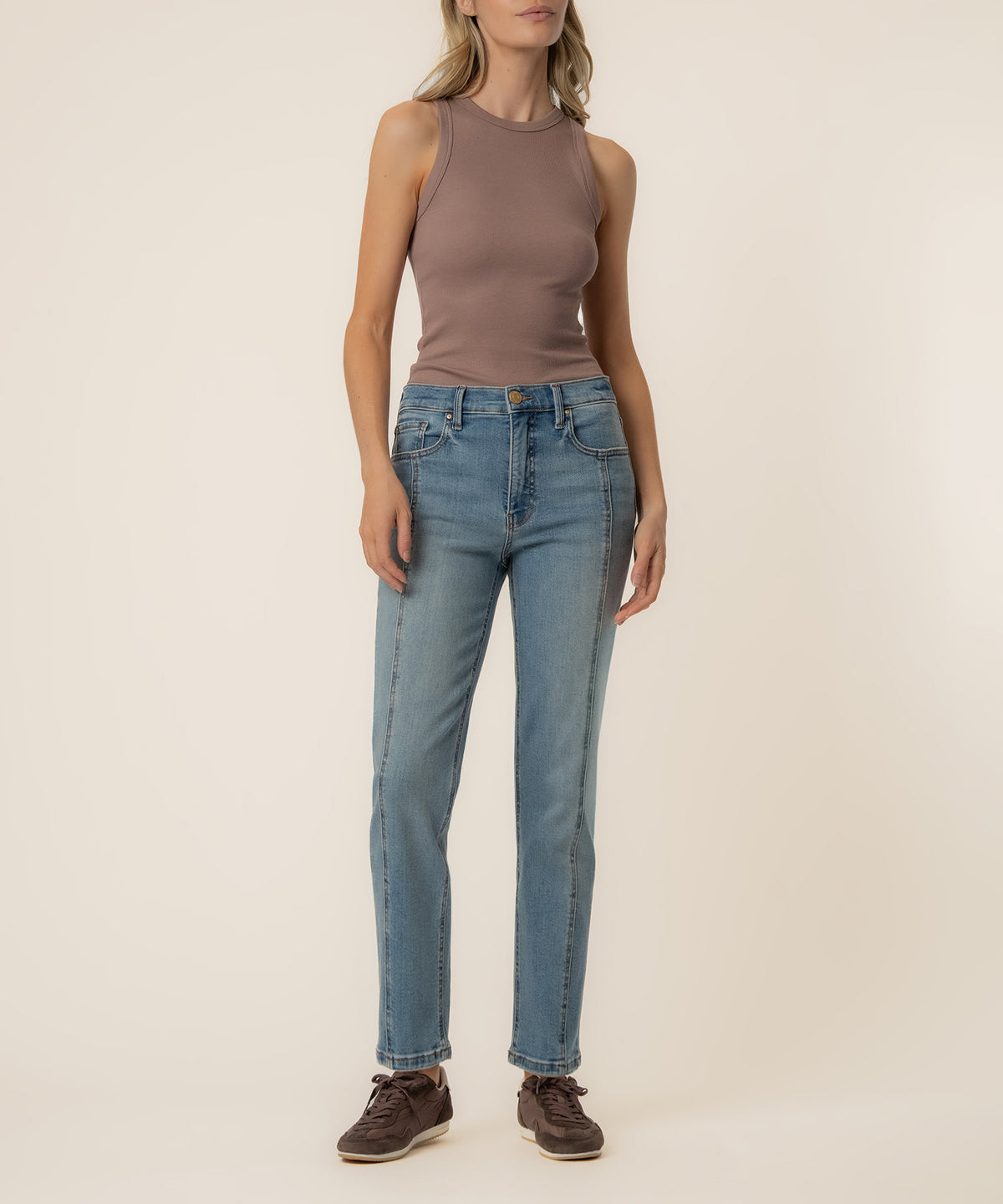Woman wearing a taupe sleeveless tank top and light blue high-rise straight-leg jeans with brown shoes.