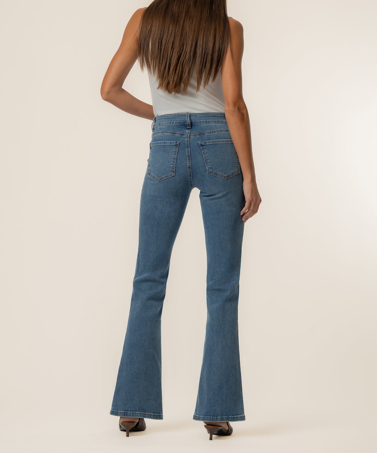 Woman wearing light blue high-rise flare jeans with a white sleeveless top, shown from back view.