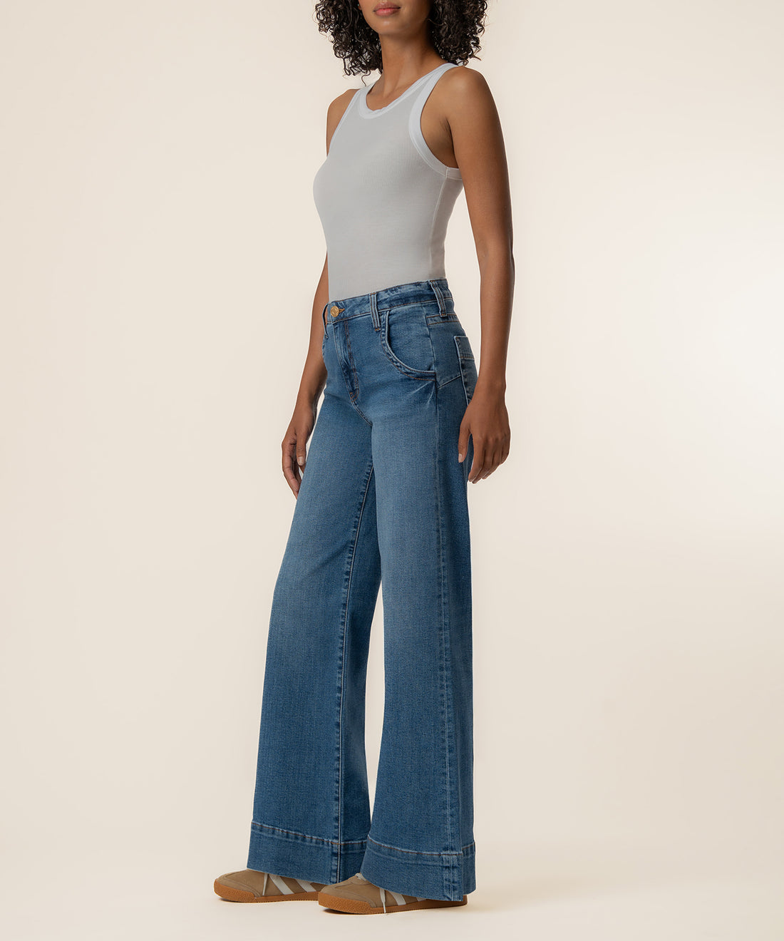 Woman wearing light gray sleeveless tank top and blue wide-leg jeans with high rise waistband and cuffed hem.
