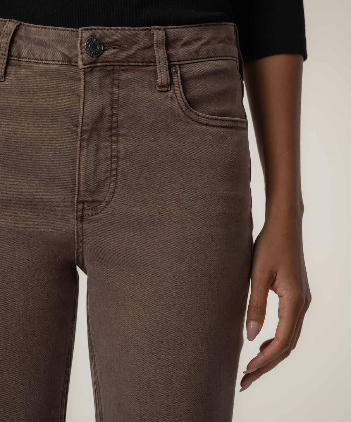Close-up of a person wearing high-rise brown twill pants with a metal button, front pocket, and a black top.