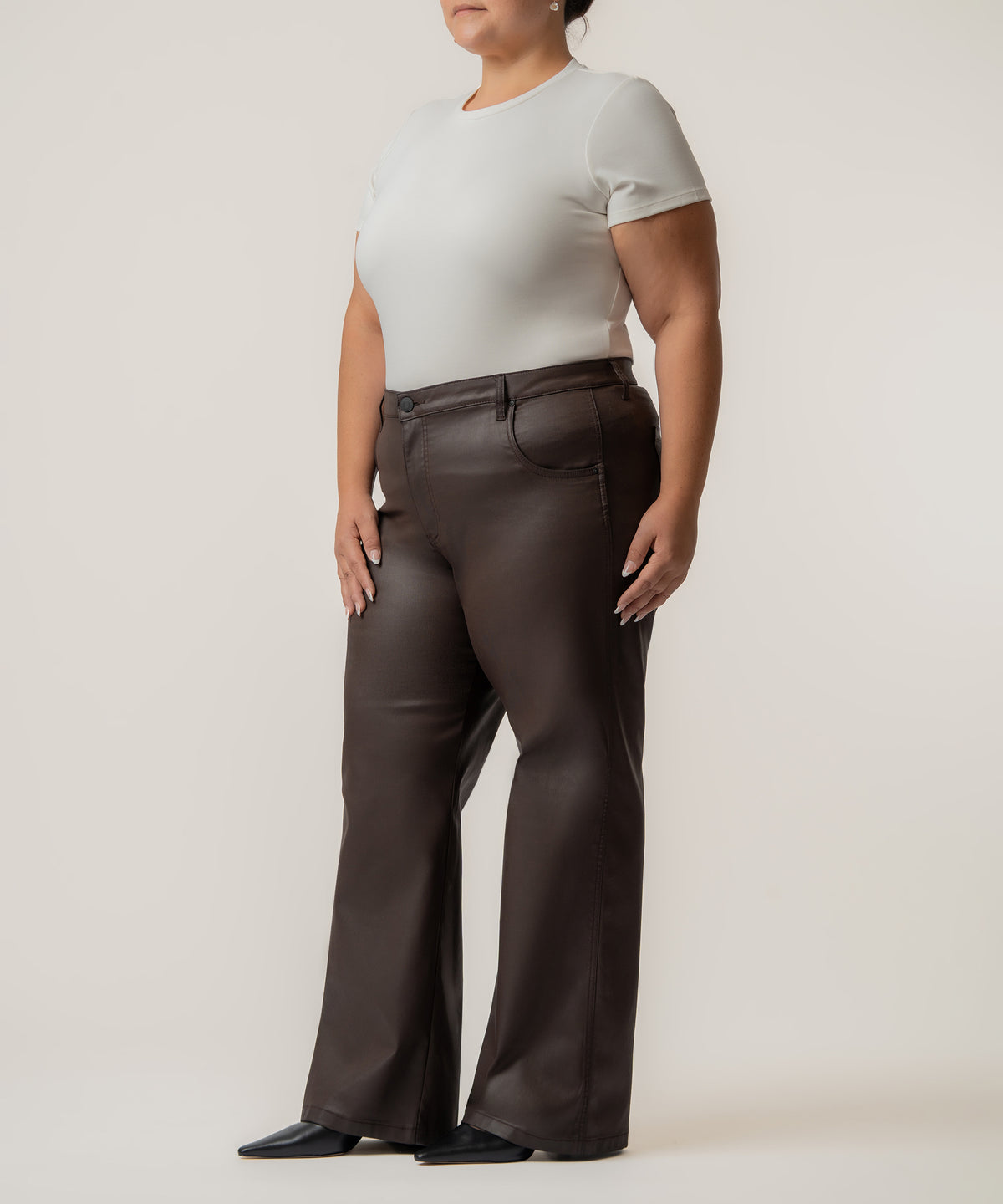 Woman wearing cream short-sleeve t-shirt and chocolate brown coated high-rise straight leg jeans.