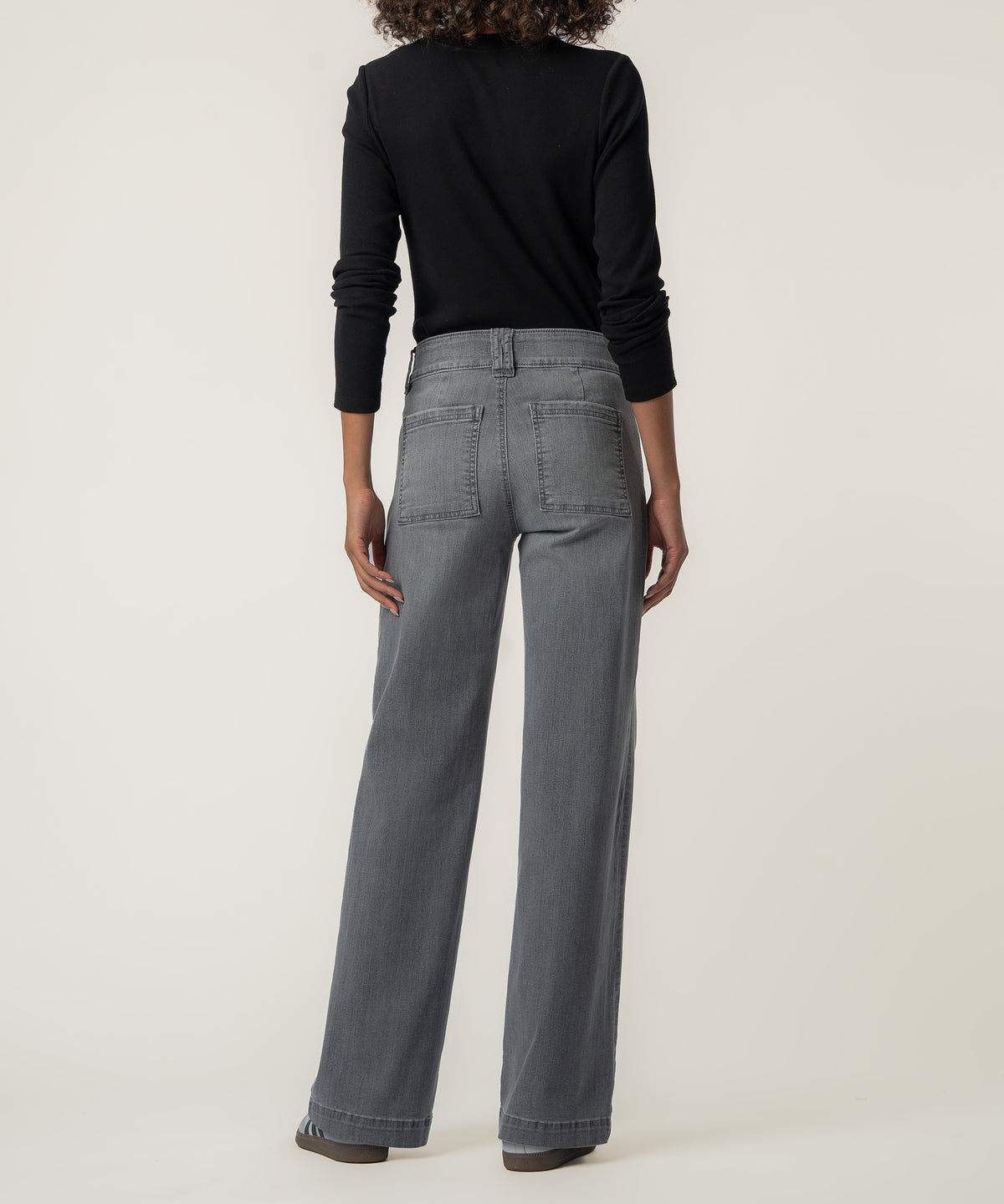 Rear view of a person wearing gray wide-leg jeans with two patch back pockets, a black long-sleeve top, and sneakers.