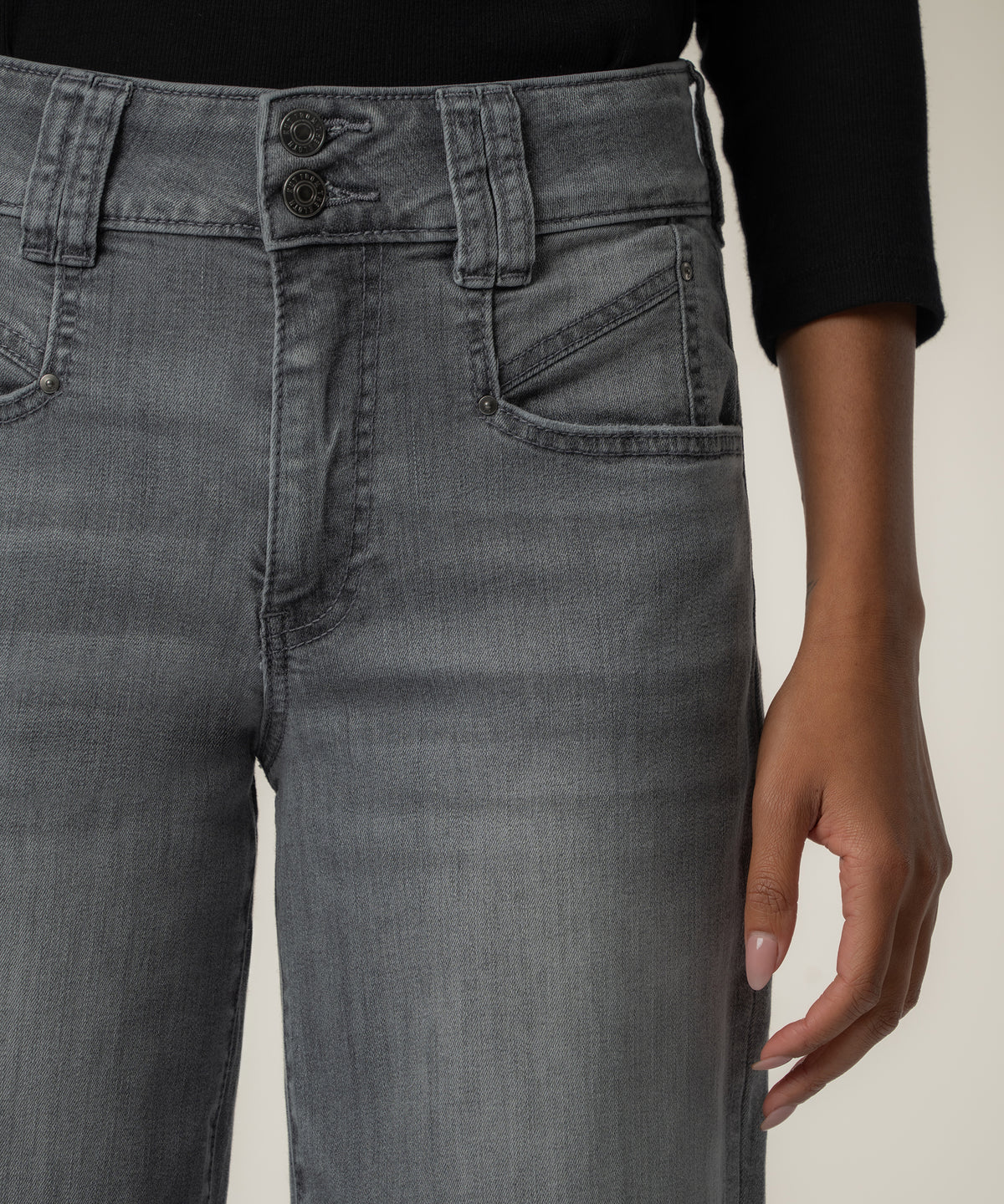 Close-up of a person wearing gray high-rise wide-leg jeans with a two-button waistband, angled front pocket, and black fitted top.