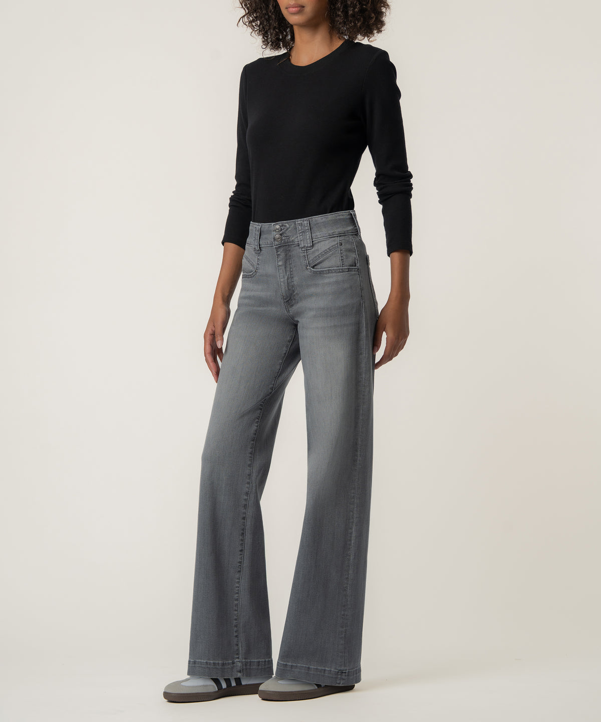 A woman wears high-rise gray wide-leg jeans with a double-button waist, a black long-sleeve top, and gray sneakers.