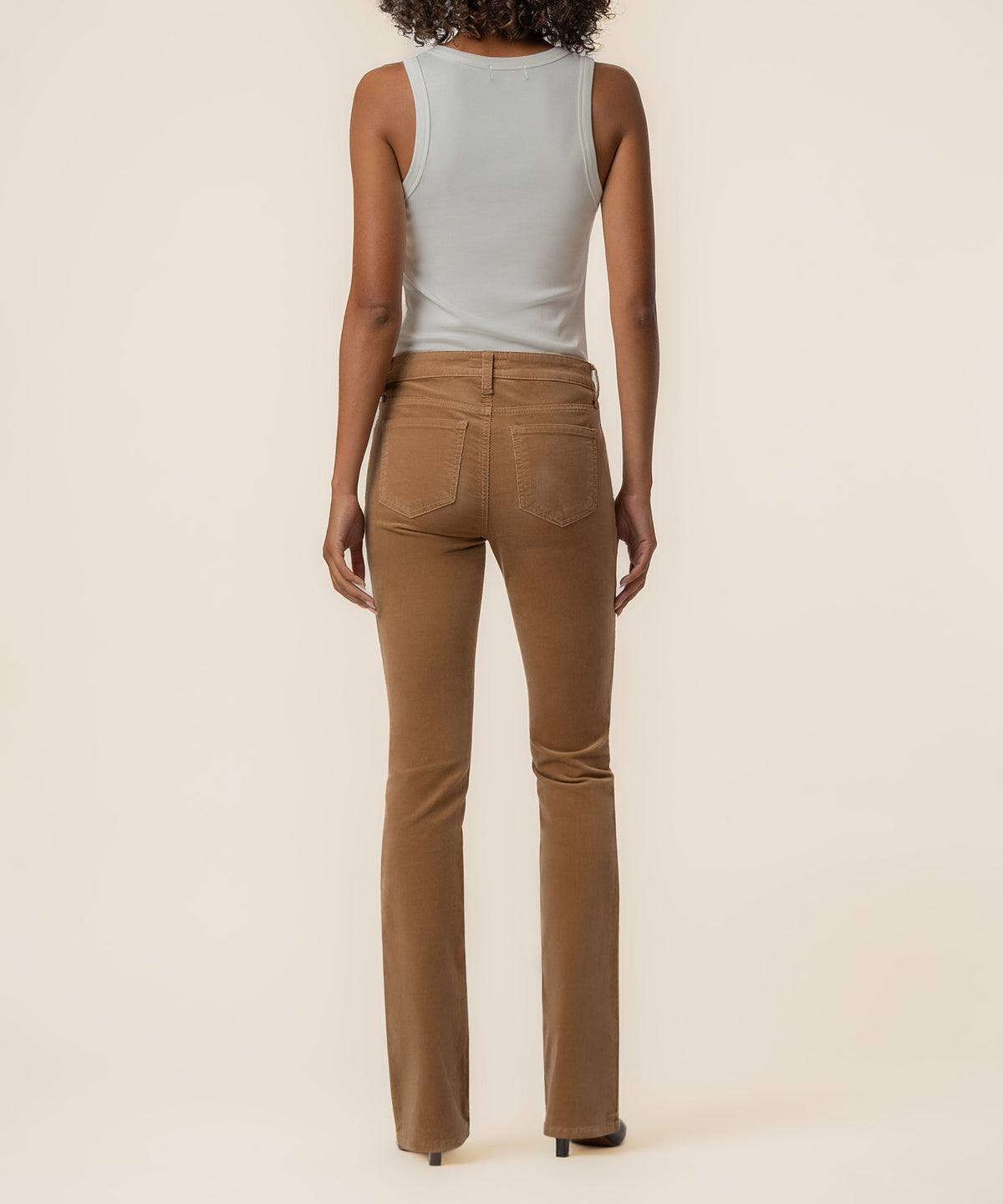 Camel corduroy bootcut pants with five-pocket styling shown from the back on a model wearing a white tank top.