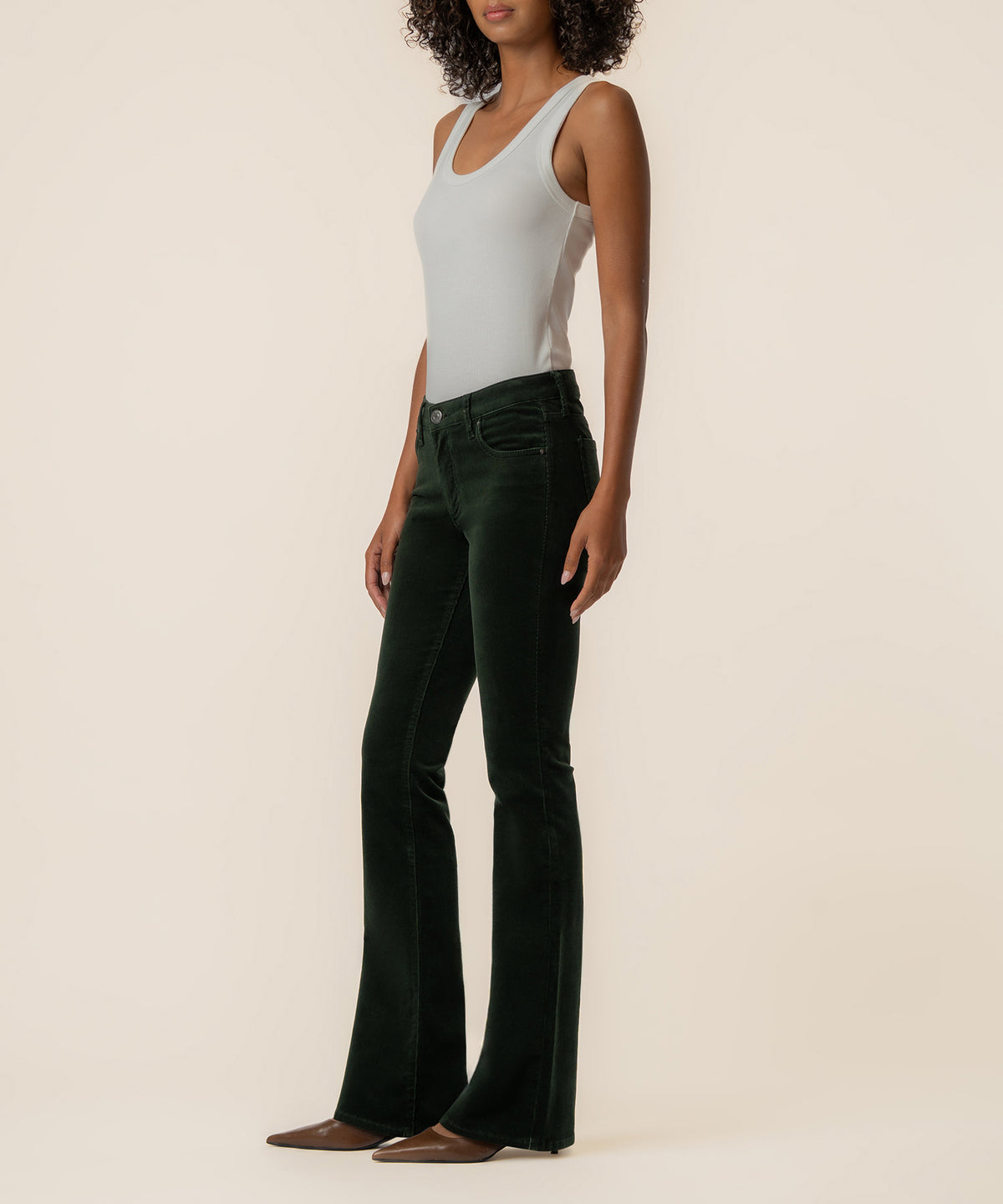 Dark forest corduroy bootcut pants with five-pocket styling and flared hem, shown on model wearing light gray tank top.