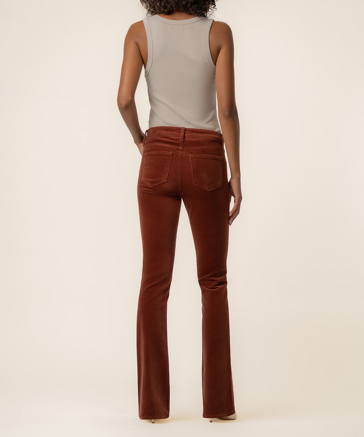 Woman wearing sienna corduroy bootcut pants with a gray sleeveless top, shown from behind.