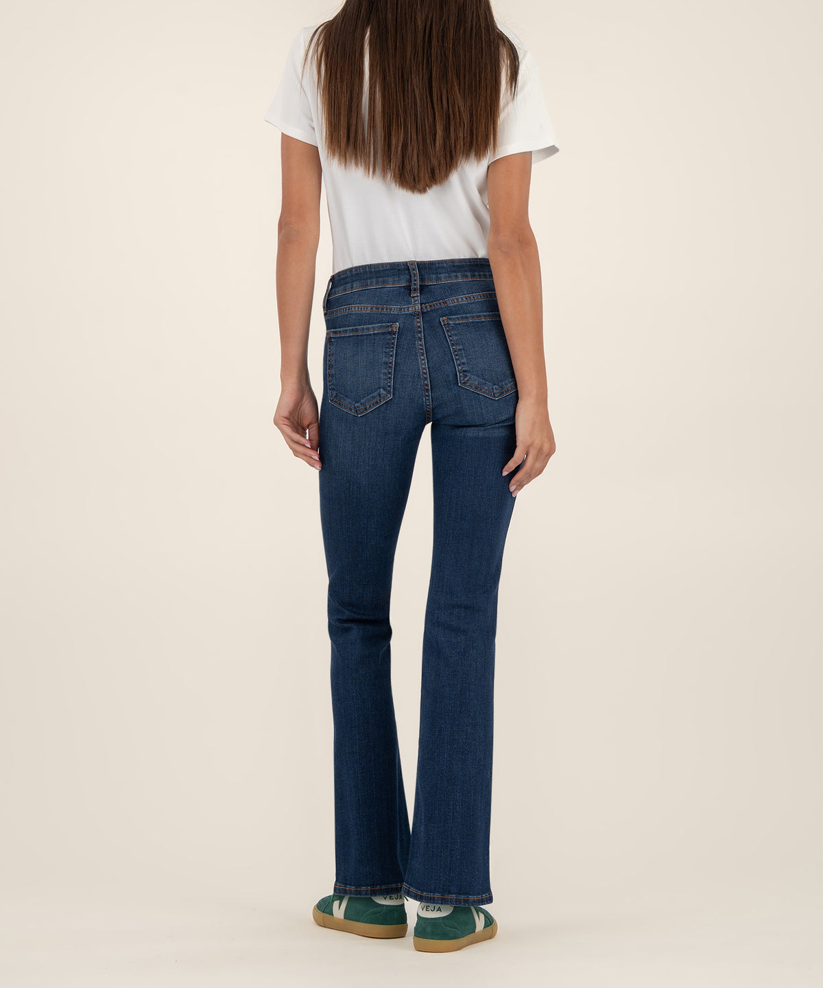 Woman wearing dark blue mid-rise bootcut jeans with white t-shirt, back view.
