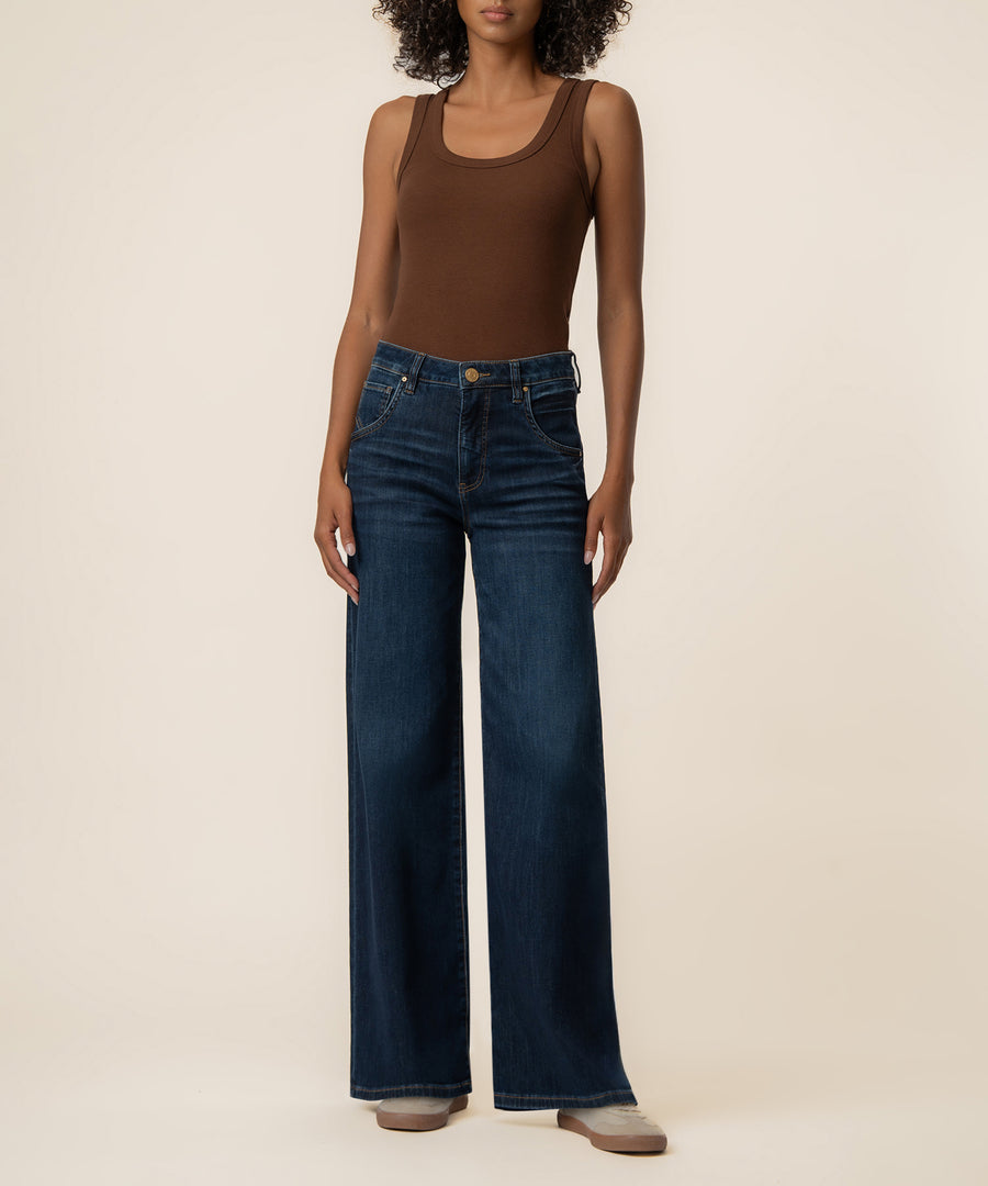 Woman wearing dark blue wide-leg jeans with high rise waistband and brown sleeveless tank top.