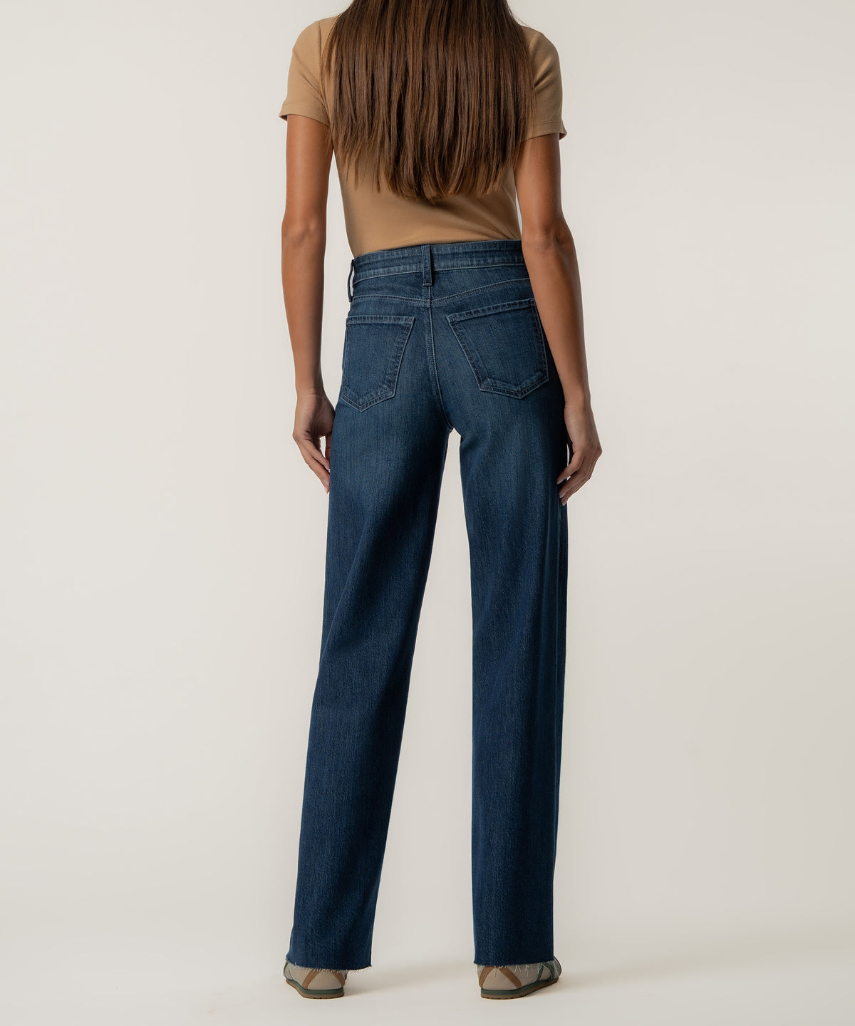 Back view of a woman wearing dark blue high-rise wide-leg jeans with raw hems and a tan short-sleeve top.