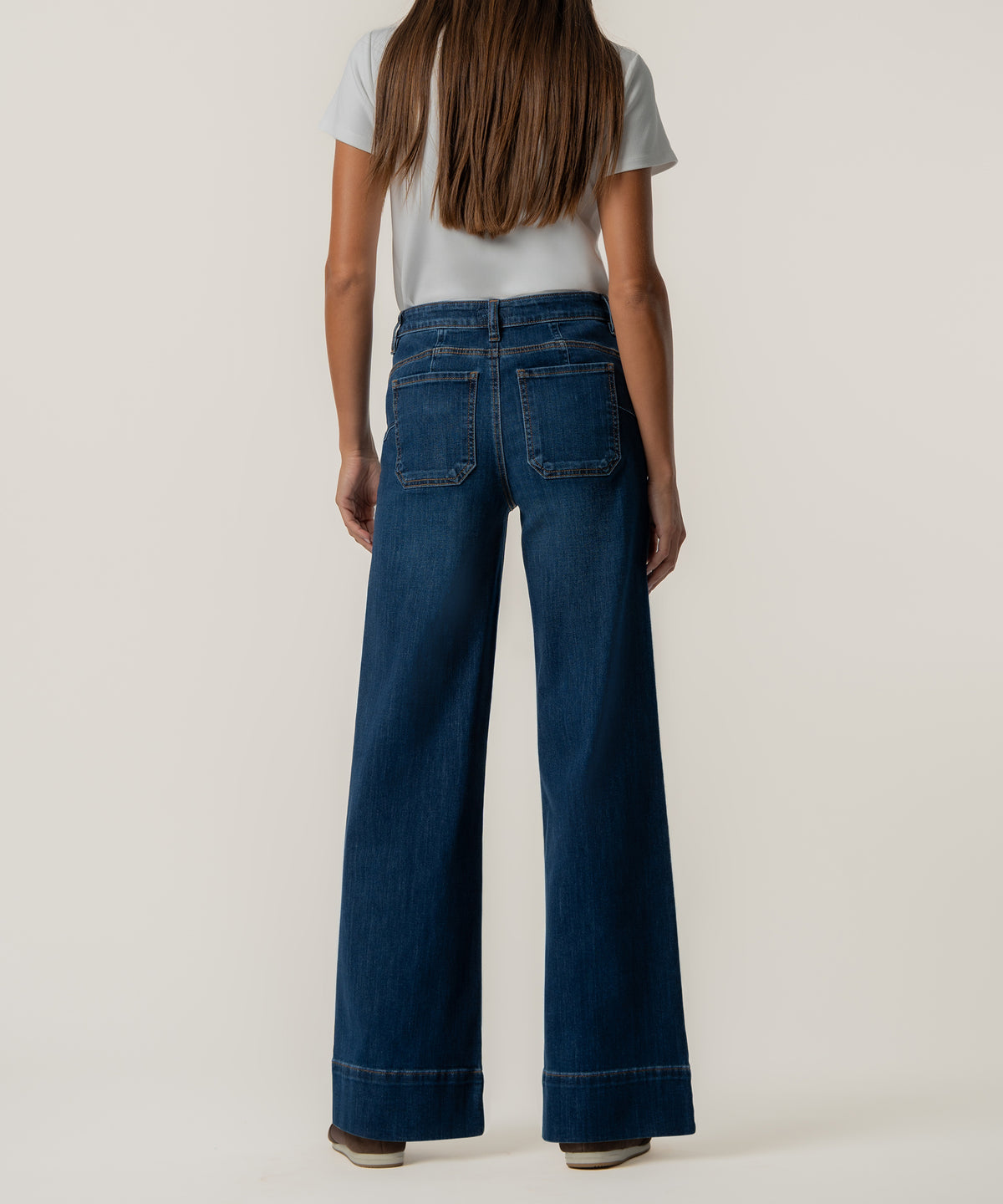 Back view of a person wearing dark blue high-rise wide-leg jeans with patch pockets, a white top, and brown shoes.