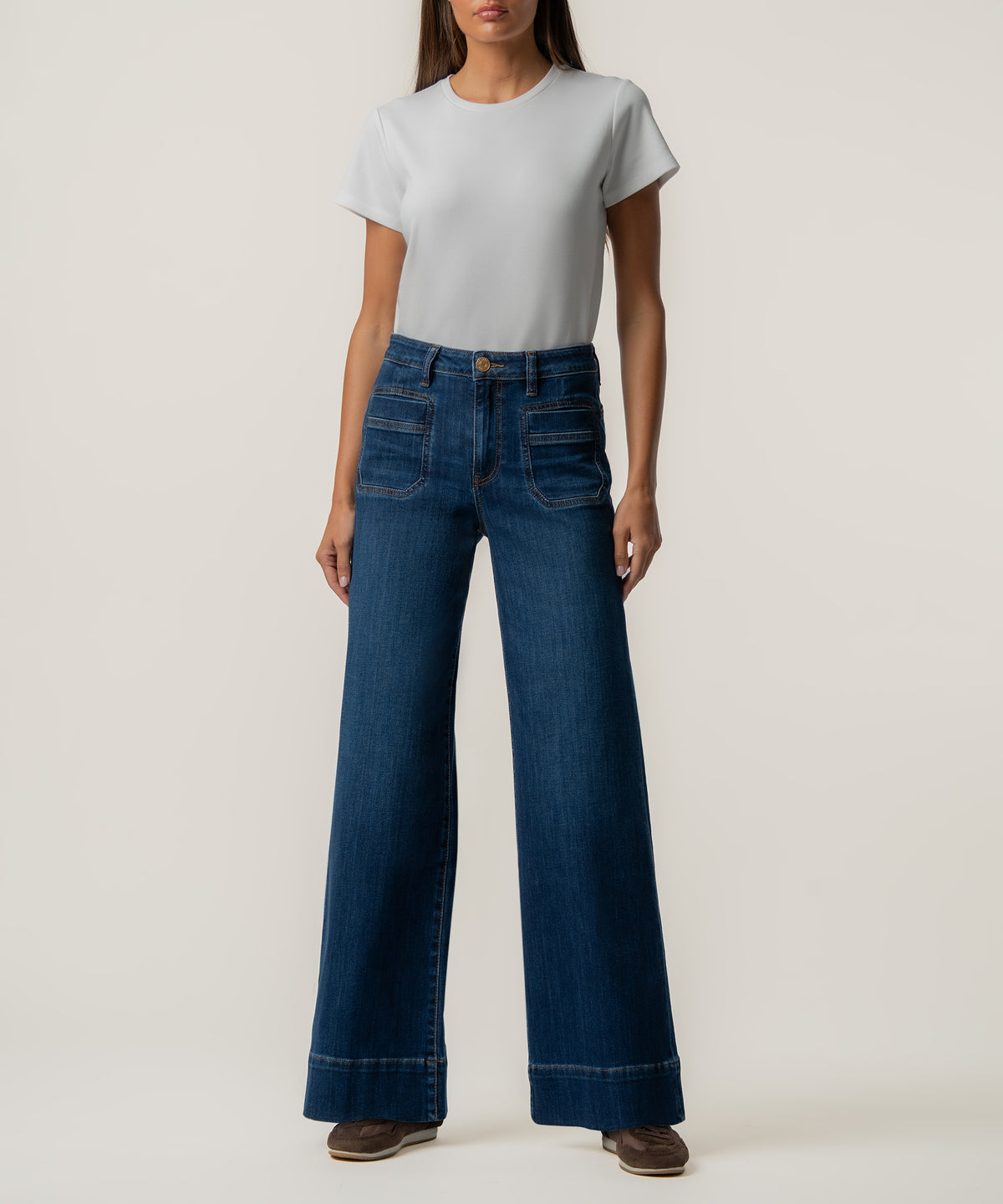 A woman wears high-rise wide-leg dark blue jeans with front patch pockets, a light gray t-shirt, and brown shoes.