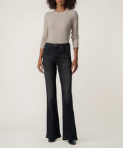 A woman stands facing forward in faded black high-rise flare jeans, a taupe long-sleeve top, and black pointed boots.