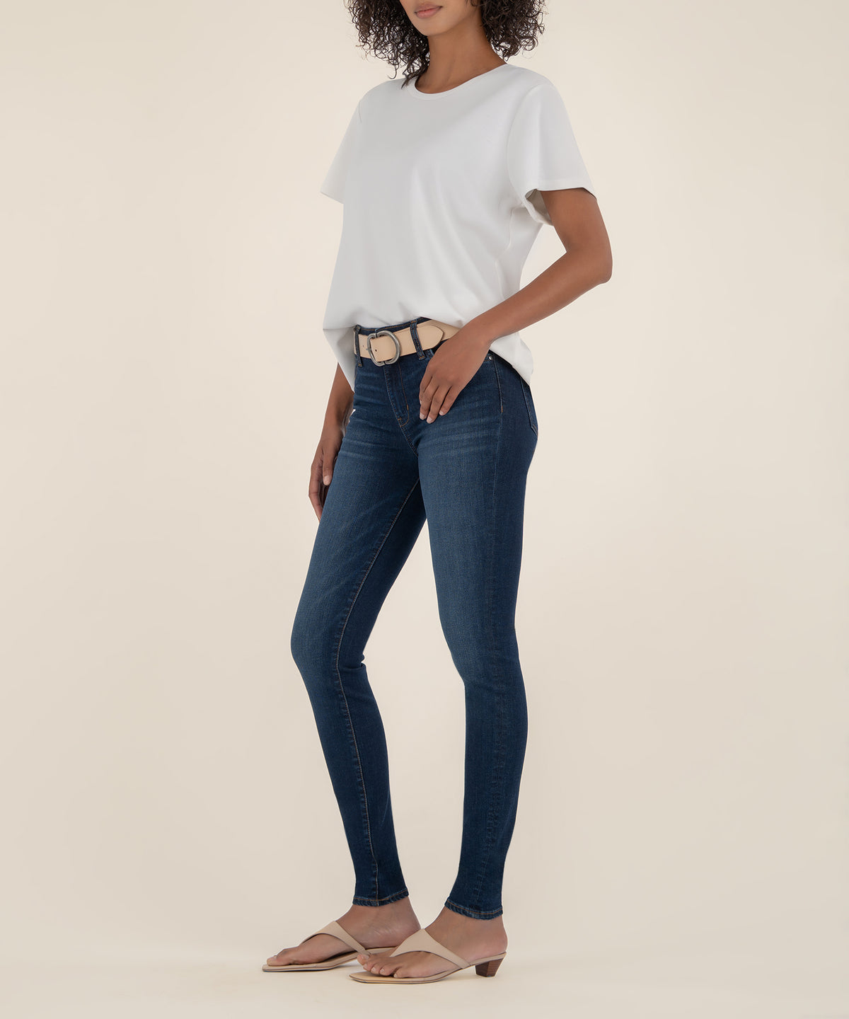 Woman wearing white t-shirt and dark blue high-rise skinny jeans with tan belt and sandals.