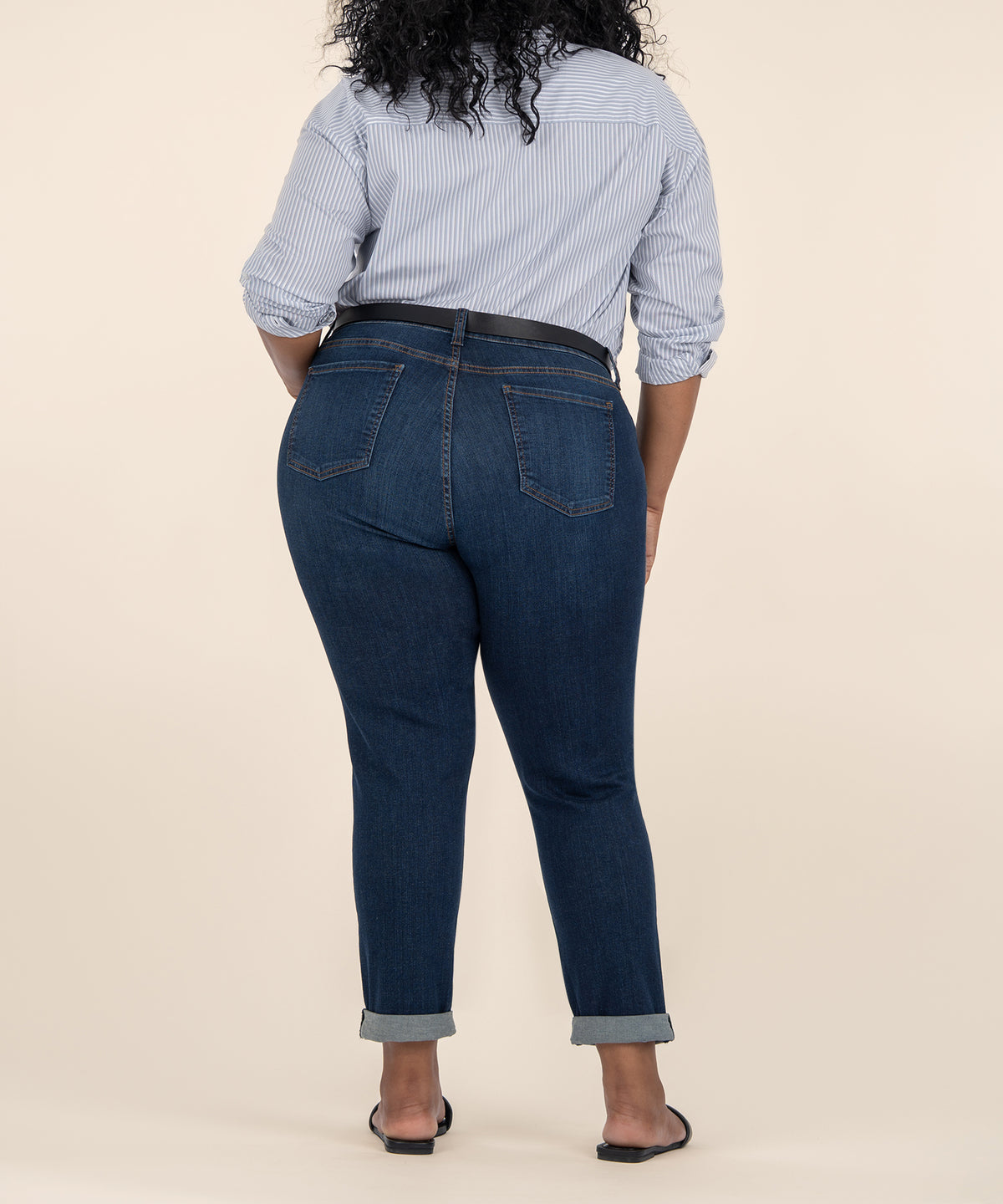 Woman wearing light blue striped button-up shirt and dark indigo boyfriend jeans with rolled cuffs, shown from behind.