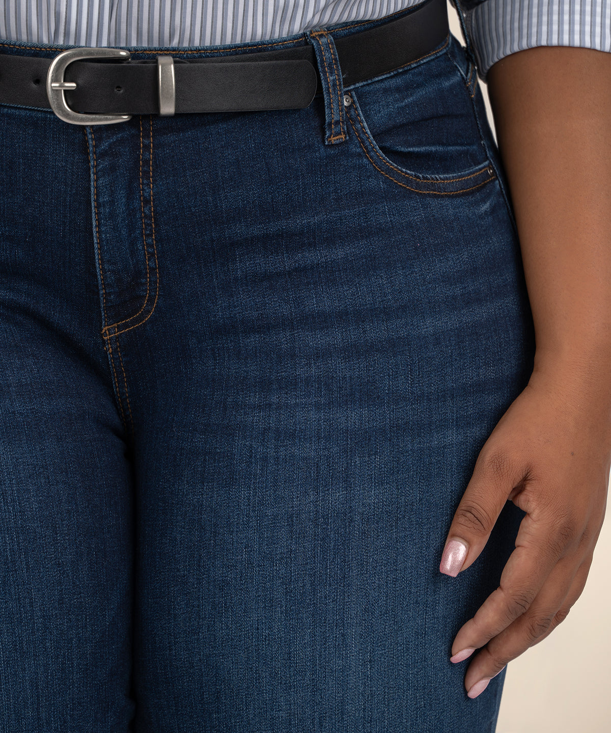 Dark indigo boyfriend jeans with black belt and orange topstitching worn with striped shirt.