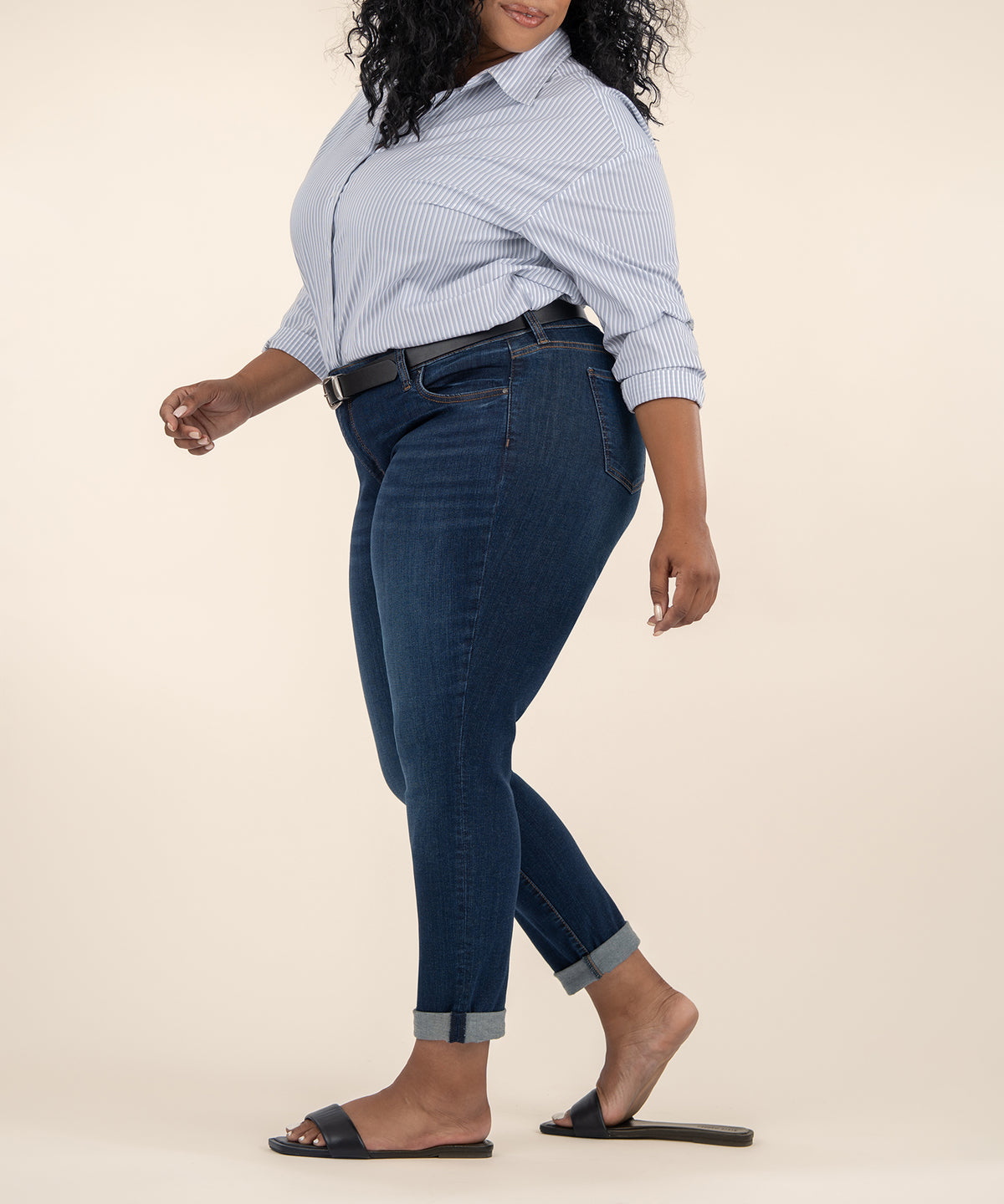 Woman wearing light blue striped button-up shirt and dark blue cuffed jeans with belt.