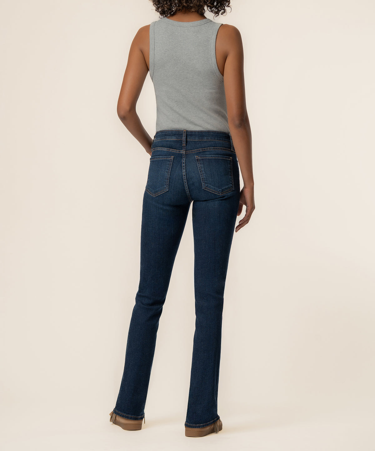 Woman wearing gray sleeveless tank top and dark blue mid-rise boyfriend jeans, shown from back.