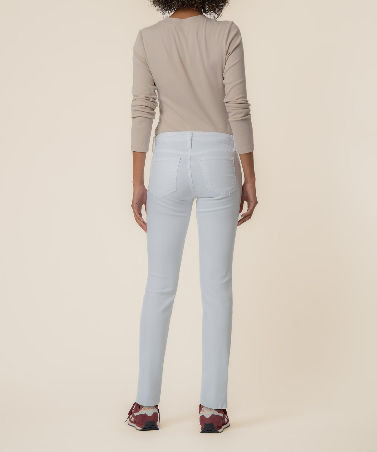 Woman wearing light blue mid-rise boyfriend jeans with visible back pockets and a beige long-sleeve top, shown from behind.