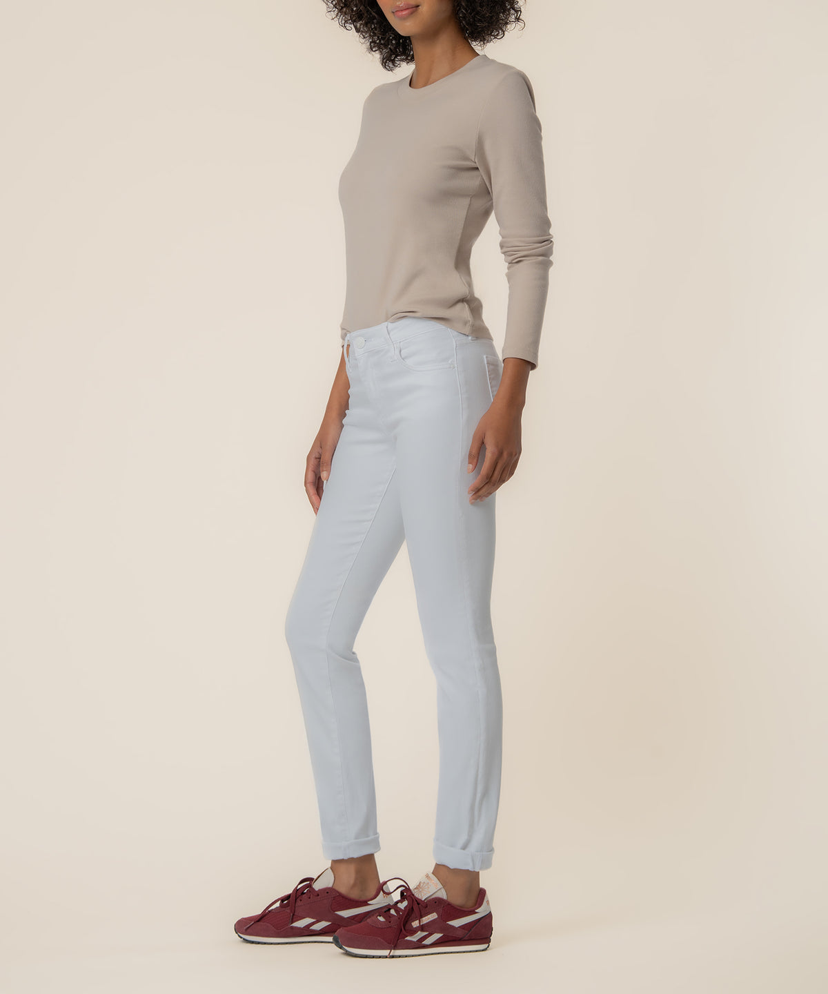 Woman wearing light blue mid-rise boyfriend jeans with a beige long-sleeve top and burgundy sneakers.