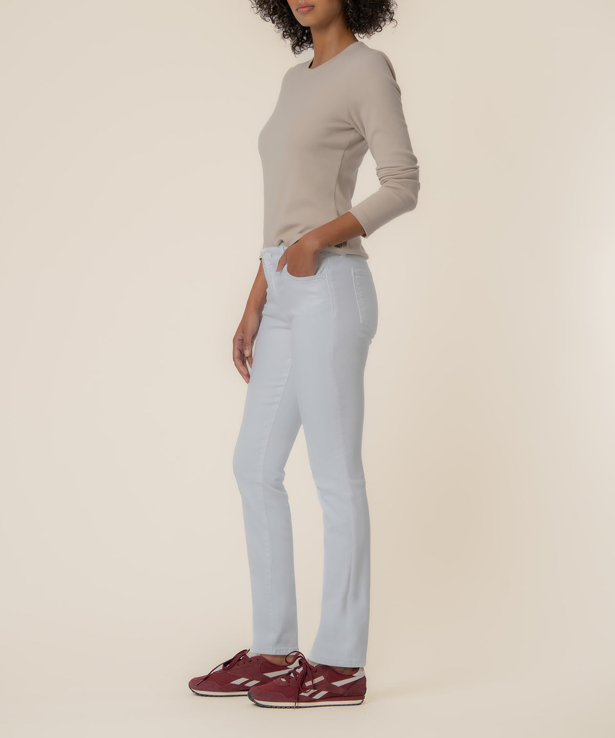 Woman wearing optic white mid-rise boyfriend jeans with a beige long-sleeve top and burgundy sneakers.