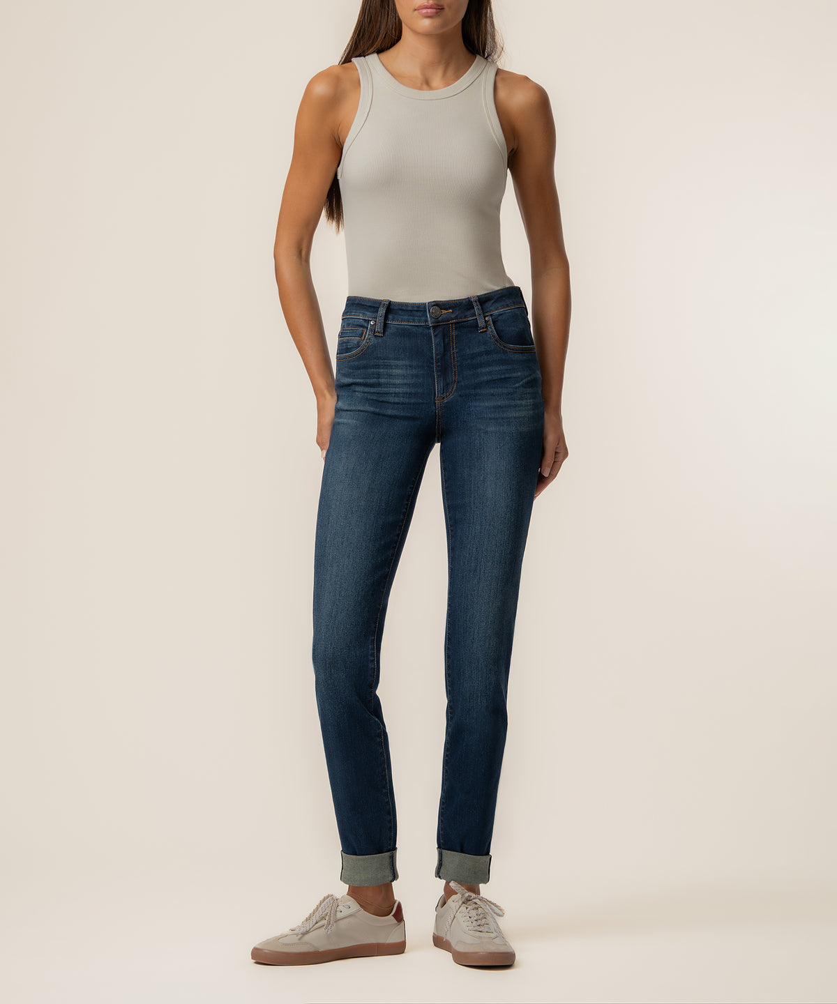 Woman wearing beige sleeveless tank top and dark blue mid-rise boyfriend jeans with rolled cuffs.