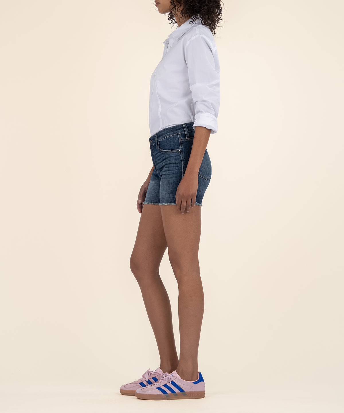 Woman wearing light blue button-up shirt and dark blue denim shorts with raw hem, paired with pink and blue sneakers.