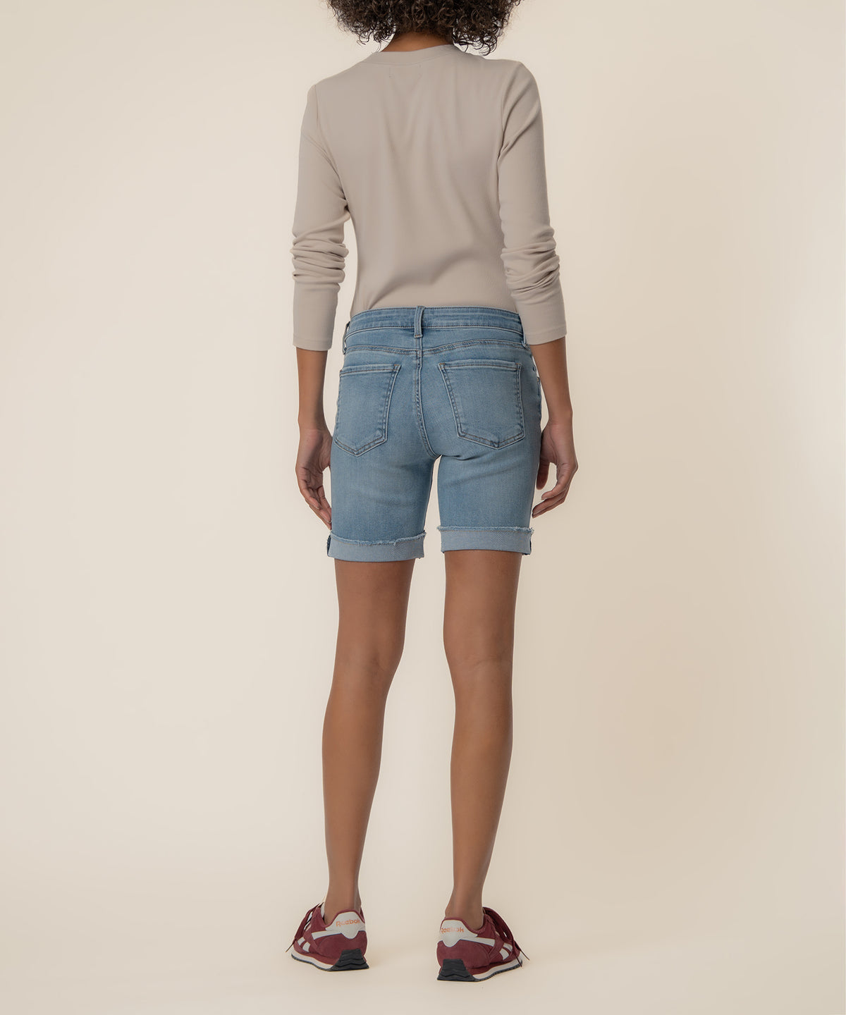 Light blue denim shorts with rolled cuffs, styled with a beige long-sleeve top and burgundy sneakers.