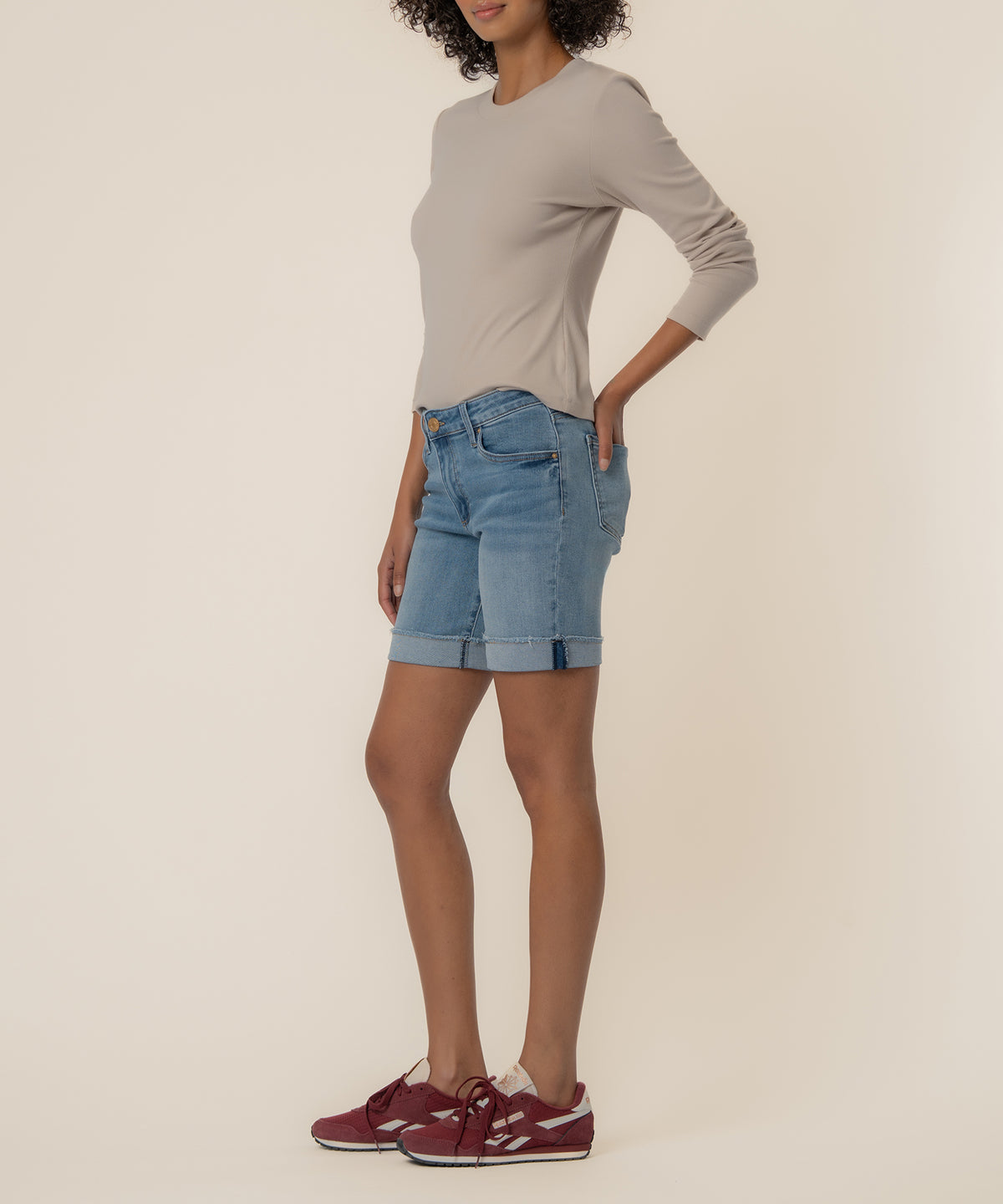 Woman wearing light gray long-sleeve top and blue denim shorts with rolled cuffs.