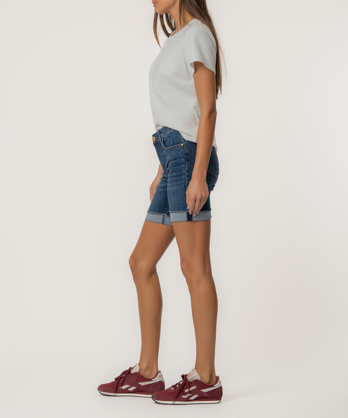 Woman wearing blue denim shorts with rolled cuffs and white t-shirt, paired with burgundy sneakers.