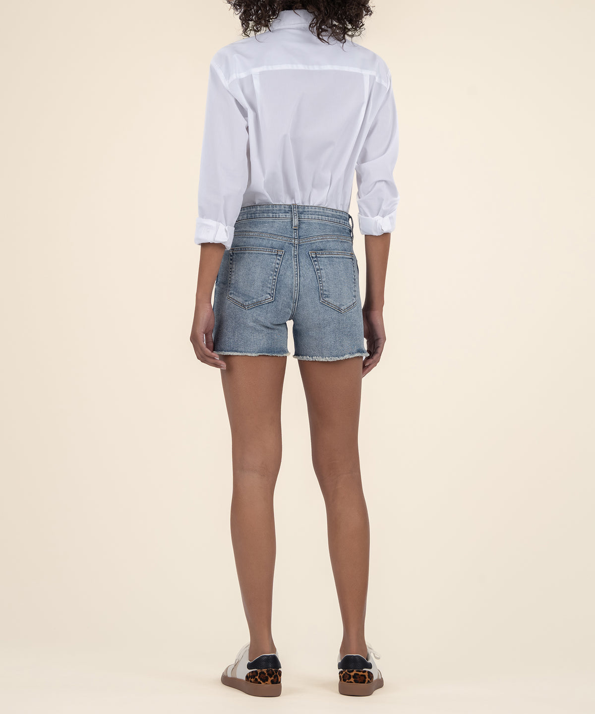 Woman wearing light blue denim shorts with frayed edges and white button-up shirt, back view.