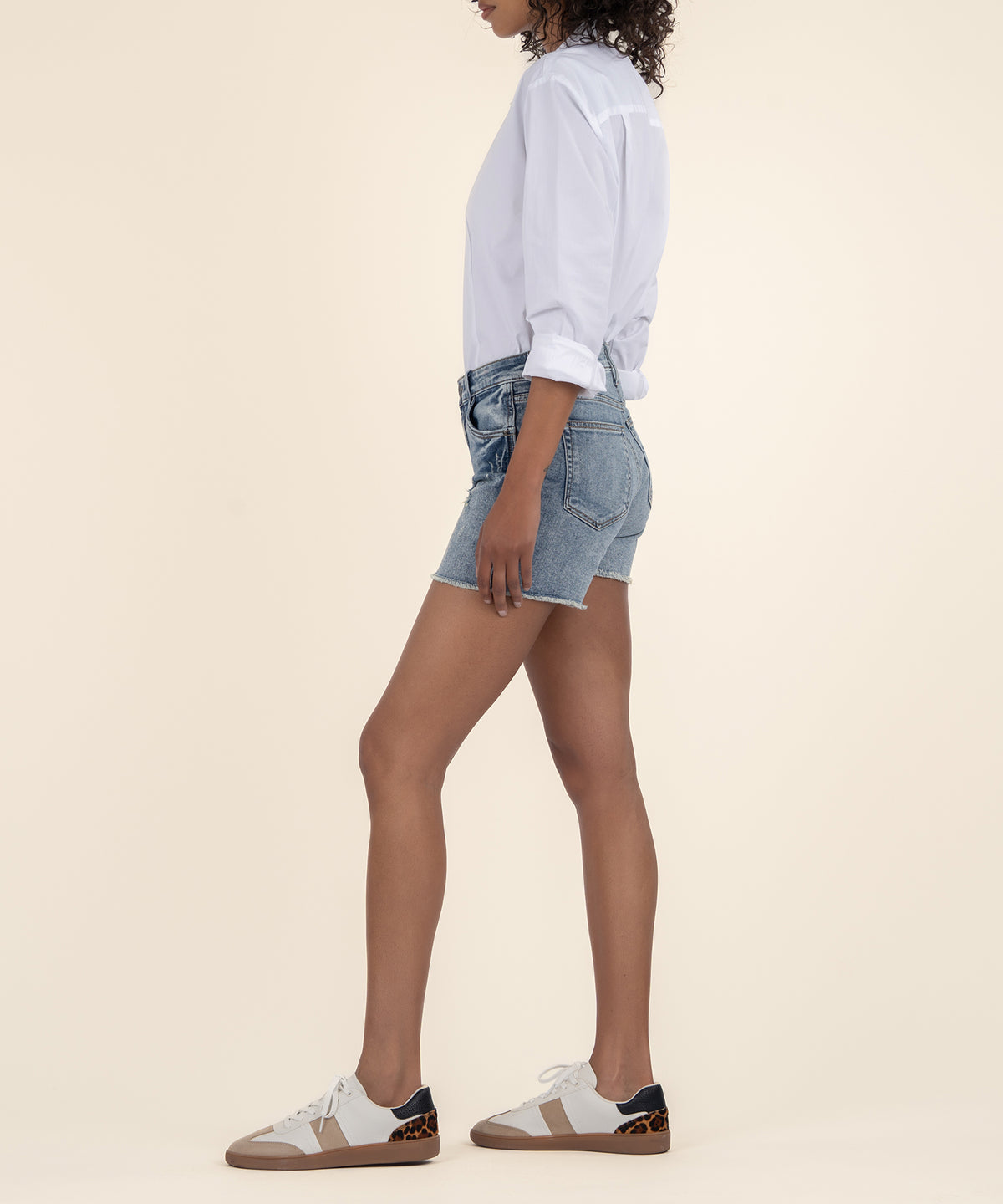 Woman wearing light blue denim shorts with high rise waistband and white button-up shirt.