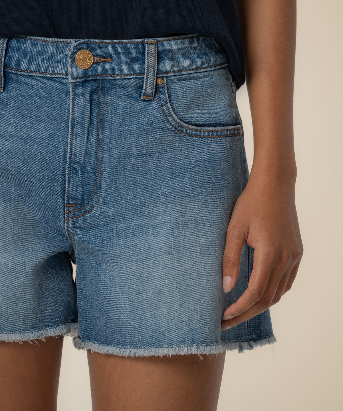 High-rise denim shorts in medium blue wash with frayed hem and gold button closure.