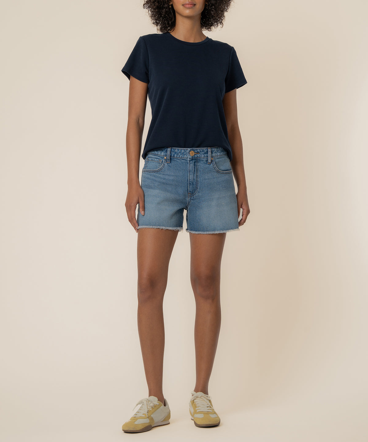 Woman wearing navy t-shirt and light blue denim high-rise shorts with frayed hem.