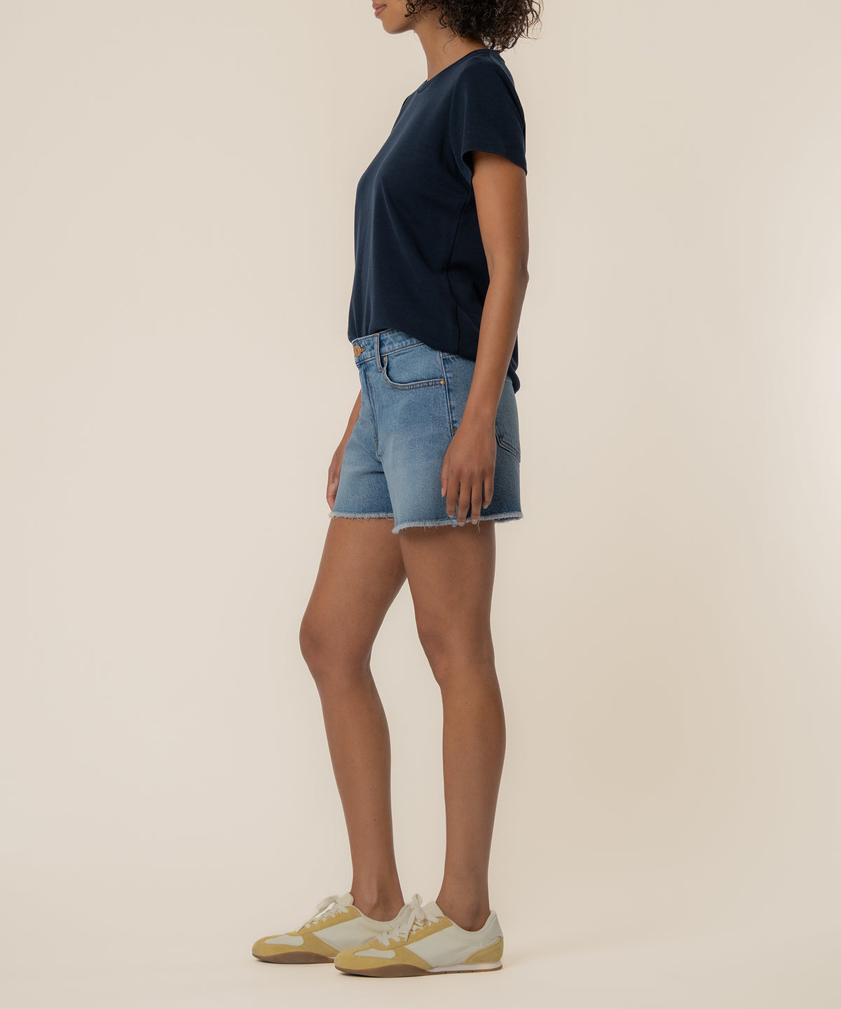 Woman wearing light blue denim high-rise shorts with frayed edges and a dark navy short-sleeve shirt.