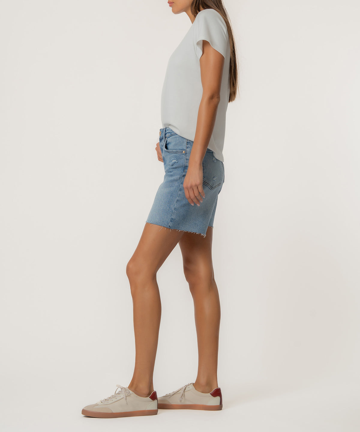 Woman wearing light blue denim high-rise shorts with frayed hem and gray t-shirt, side view.