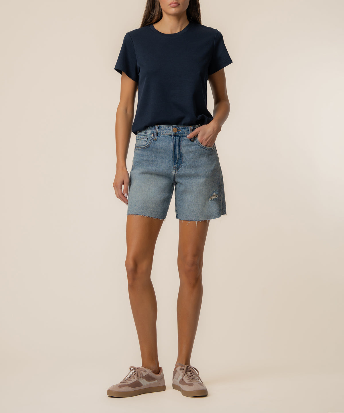Woman wearing navy t-shirt and light blue denim shorts with distressed details and raw hem.