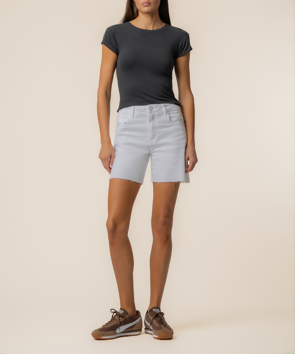 White high-rise denim shorts with frayed hem, worn with black t-shirt and brown sneakers.