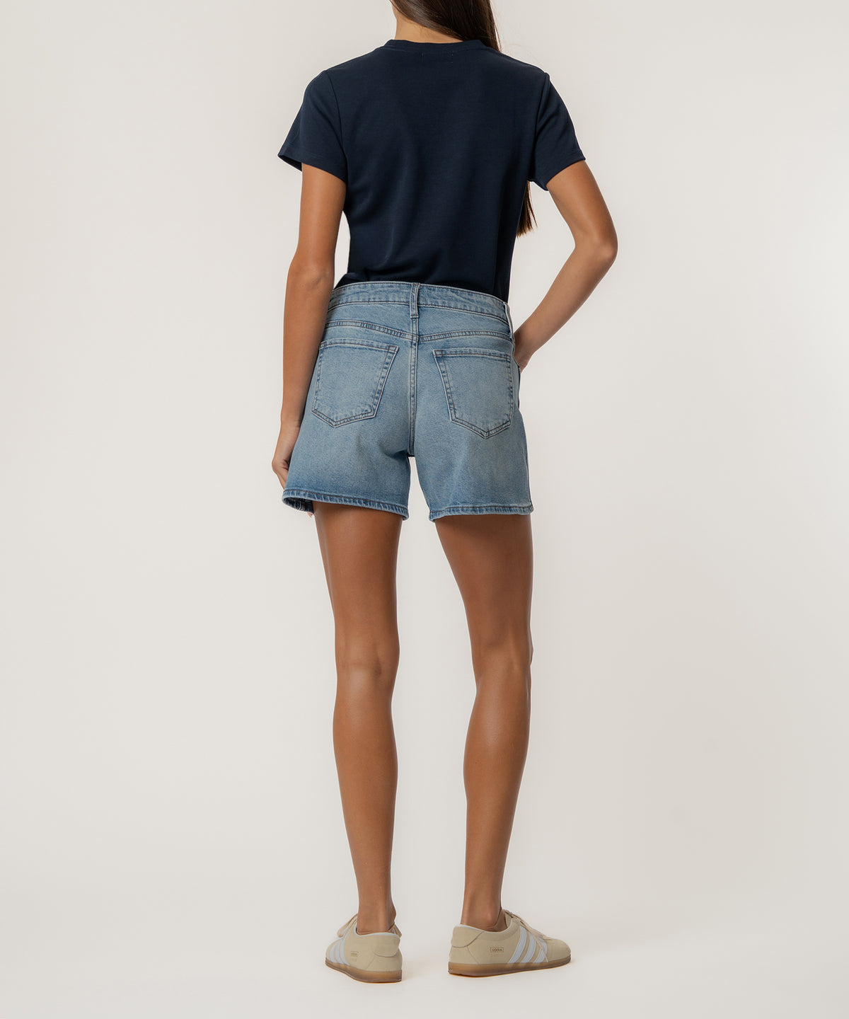 Woman wearing light blue denim high-rise shorts with a navy t-shirt, shown from behind.