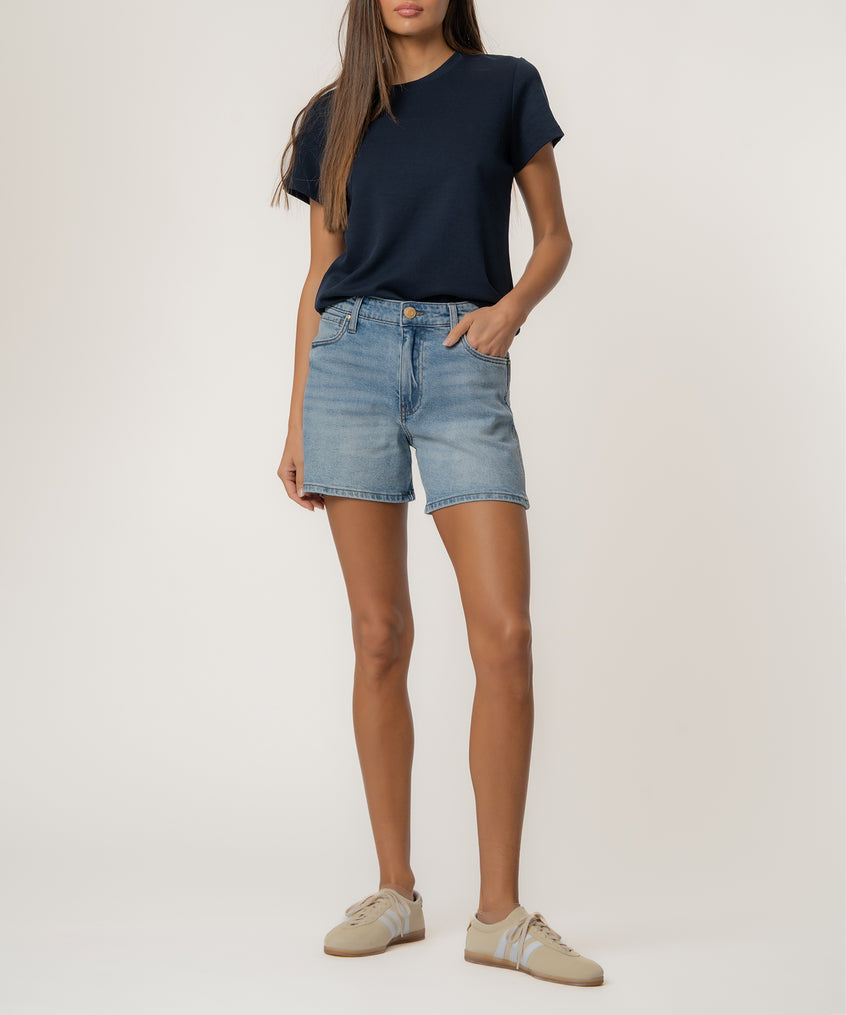 Light blue denim high-rise shorts with frayed hem paired with dark navy t-shirt and cream sneakers.
