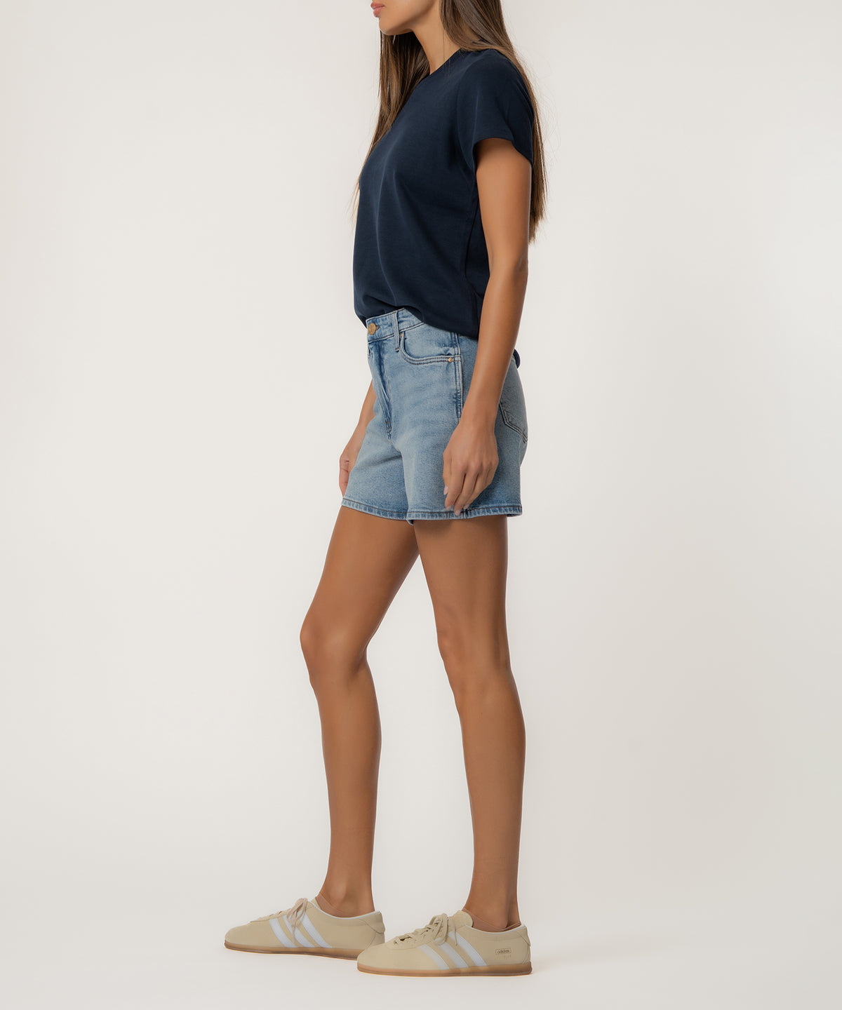 Woman wearing light blue denim high-rise shorts with a dark navy t-shirt and cream sneakers.