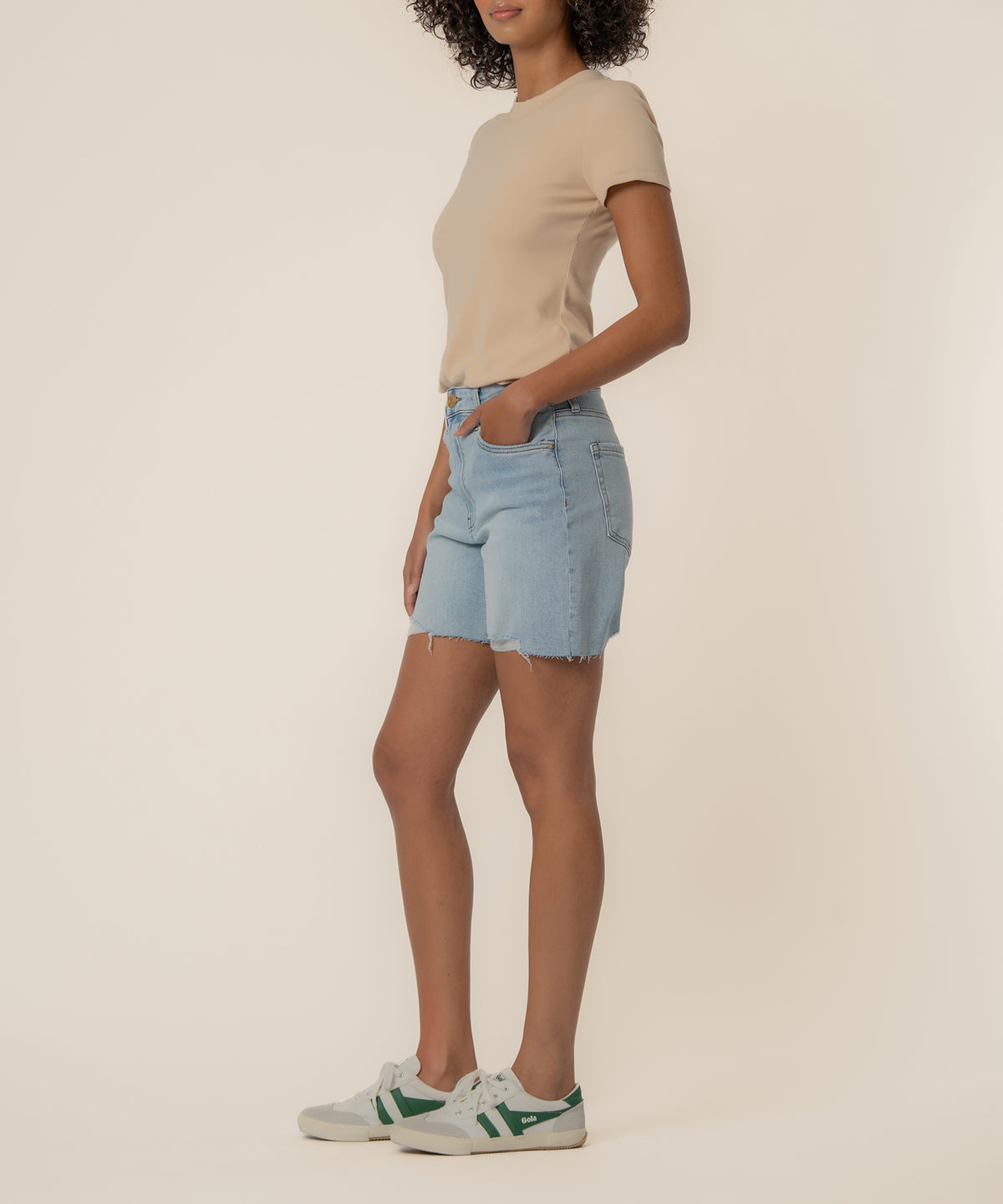 Woman wearing light blue denim shorts with distressed edges and a beige short-sleeve t-shirt.