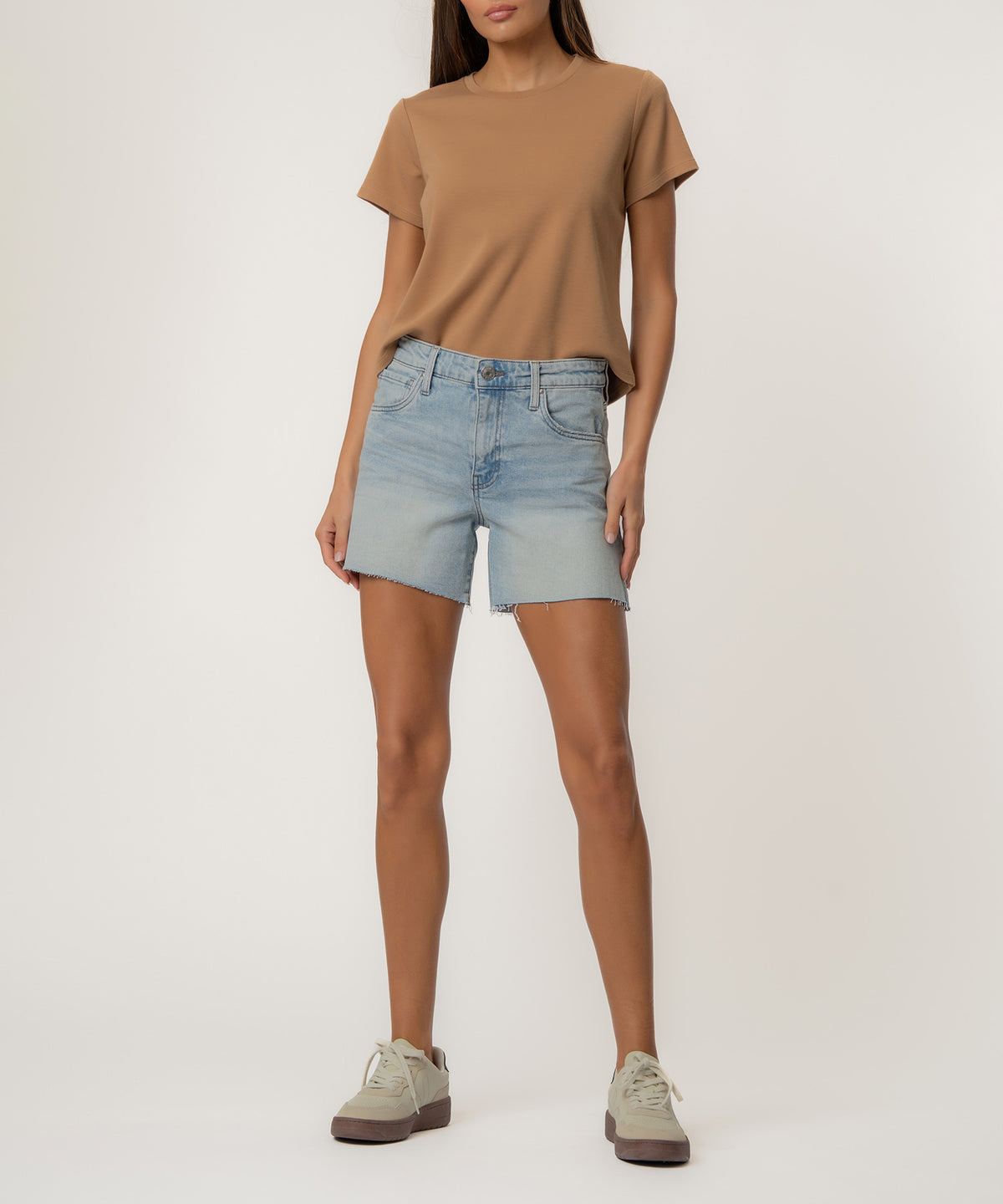Woman wearing tan t-shirt and light blue denim shorts with distressed edges and high waistband.
