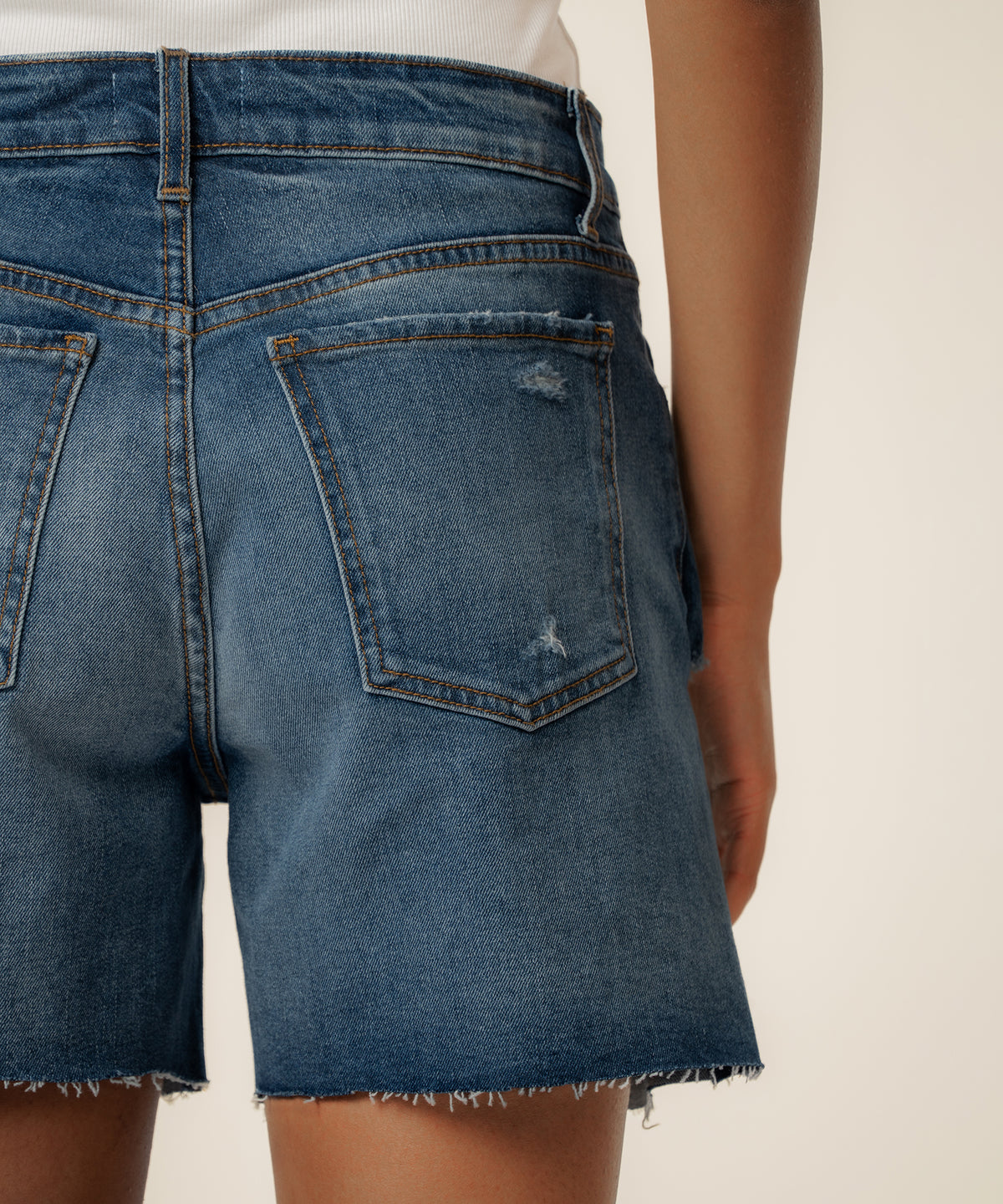 High-rise denim shorts in medium blue wash with distressed details and raw-cut hem.