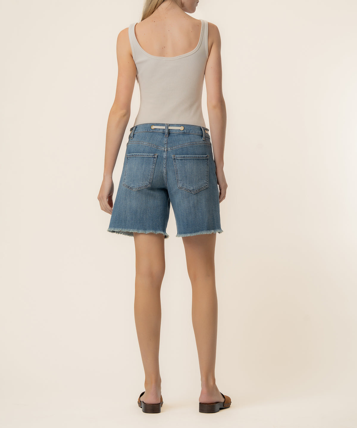 Woman wearing light gray tank top and blue denim high-rise shorts with frayed hem, viewed from back.