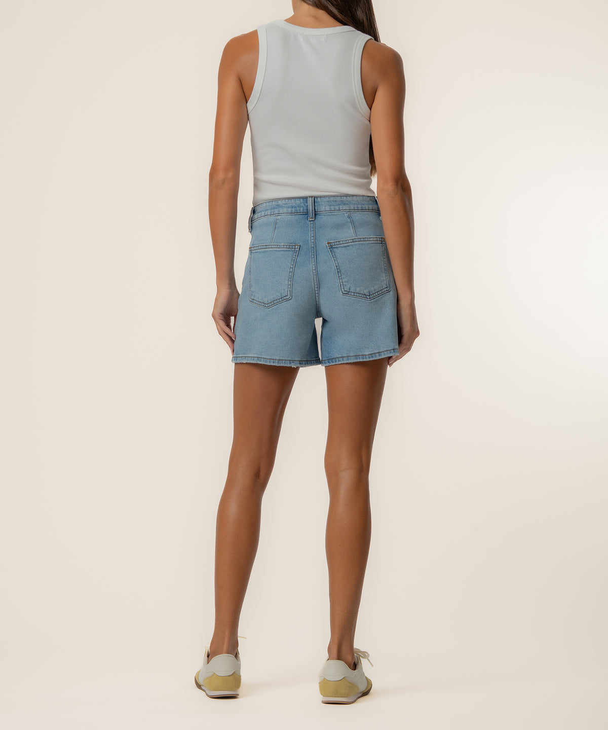 Woman wearing light blue denim shorts with high rise waistband and white sleeveless tank top, shown from back view.