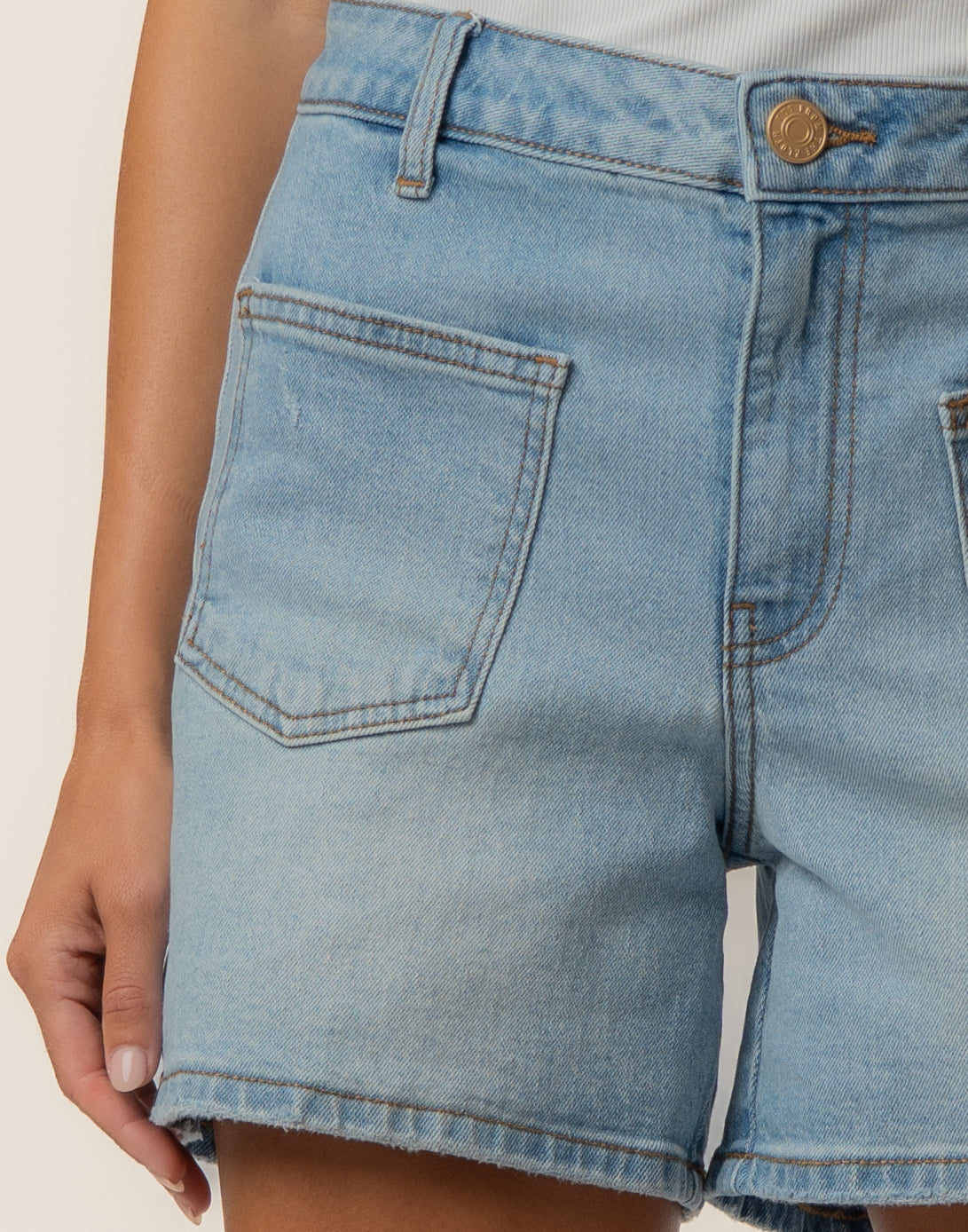 Light wash denim shorts with high rise waist, brass button, and front patch pocket visible on model.